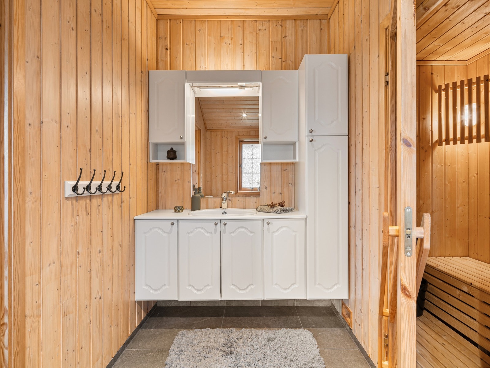 Badet har naturlig panel på veggene og grå fliser på gulv med gulvvarme. Galleribilde