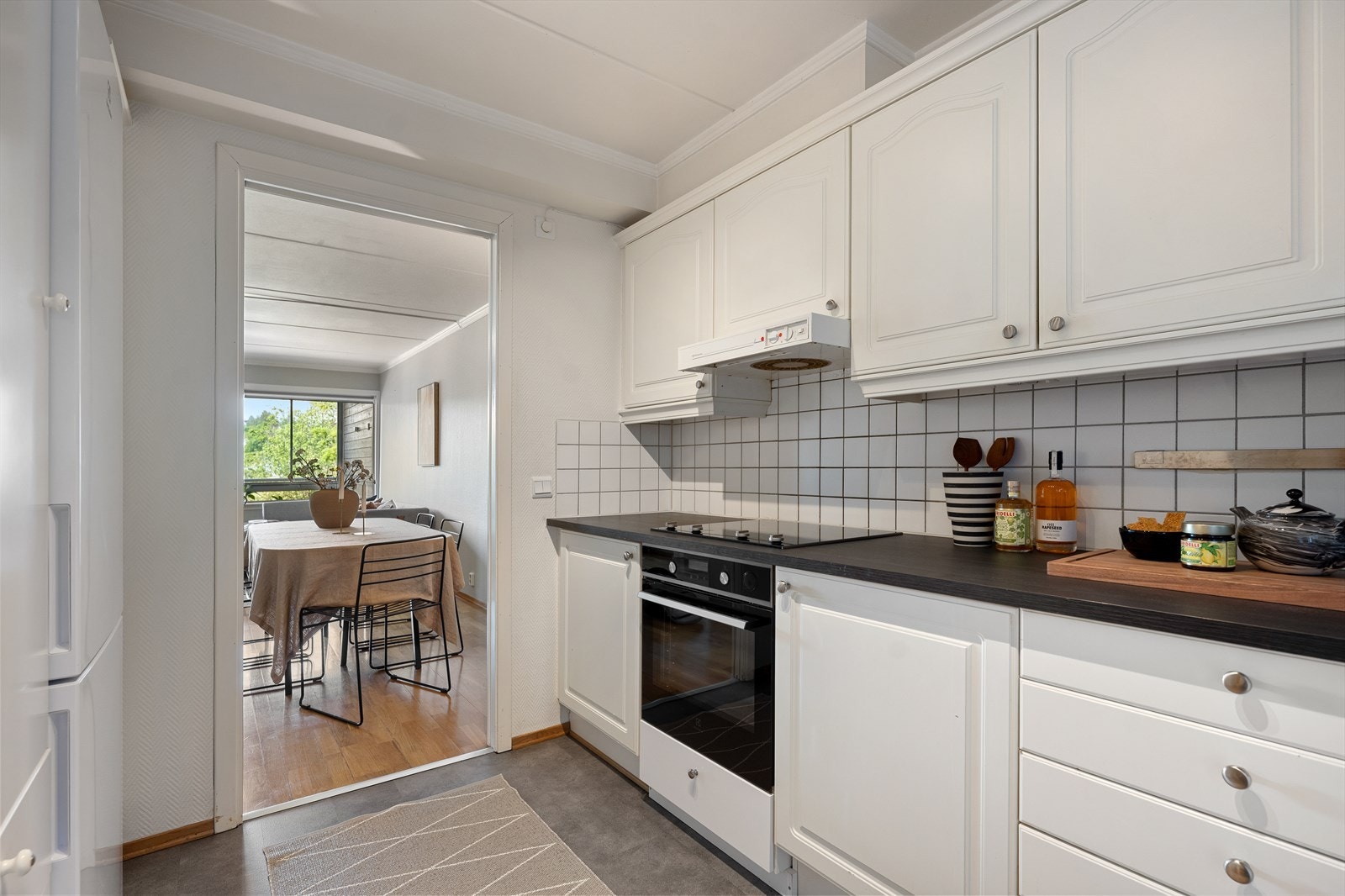 Innredningen består av en delvis eldre kjøkkenløsning kombinert med noe oppgradert IKEA-kjøkkeninnredning med hvite glatte og ett-speils profilerte fronter. Mørk laminatbenkeplate gir en fin kontrast til de lyse skapfrontene. Galleribilde