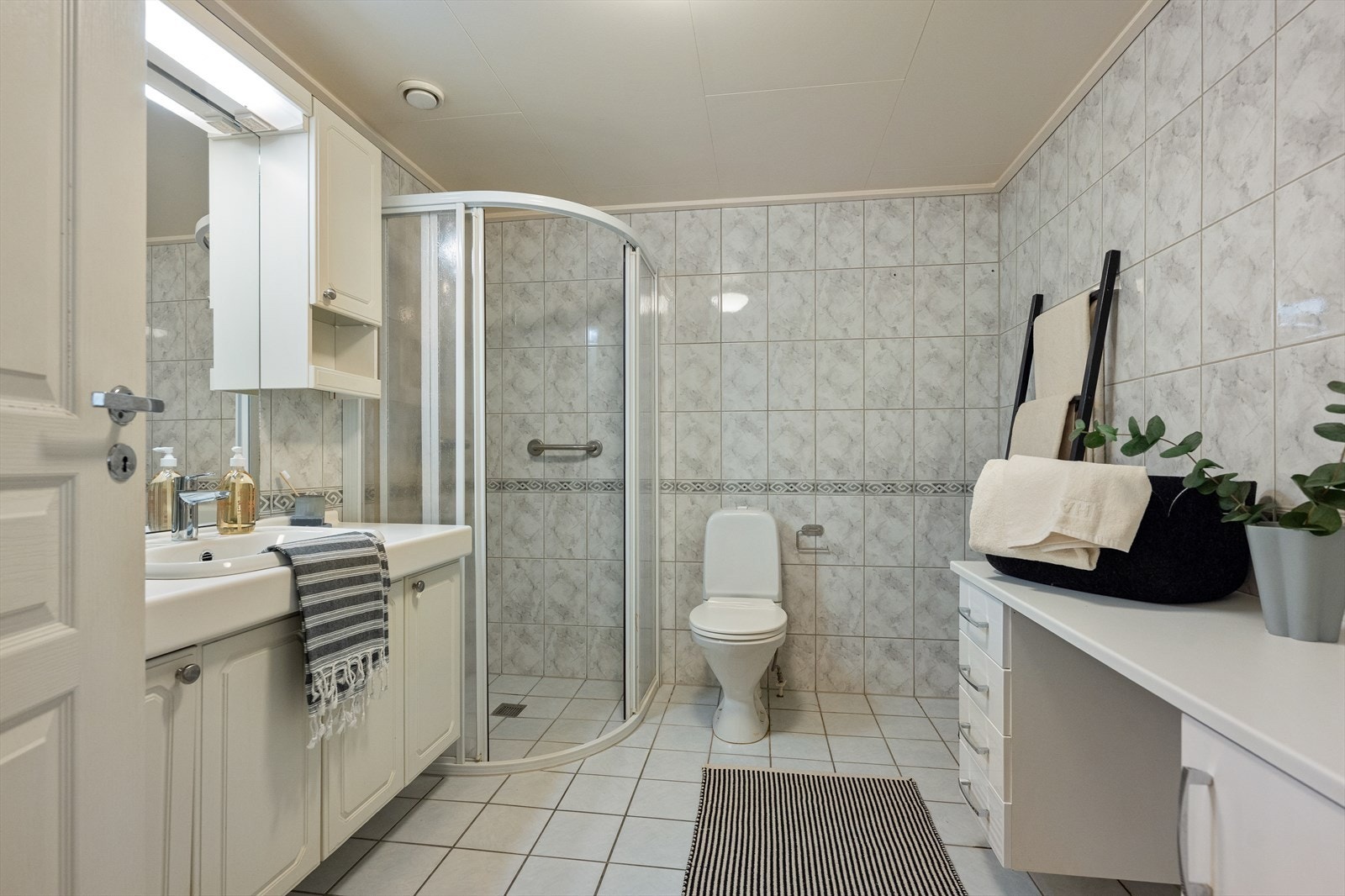 Badet er romslig og innredet med fliser på gulv og vegger, samt Takess-plater i himlingen. Det er varme i gulvet. Badet er utstyrt med toalett, dusjhjørne med gulvskinne, skyvedører og ett-greps krummet dusjarmatur fra Celeste. Galleribilde
