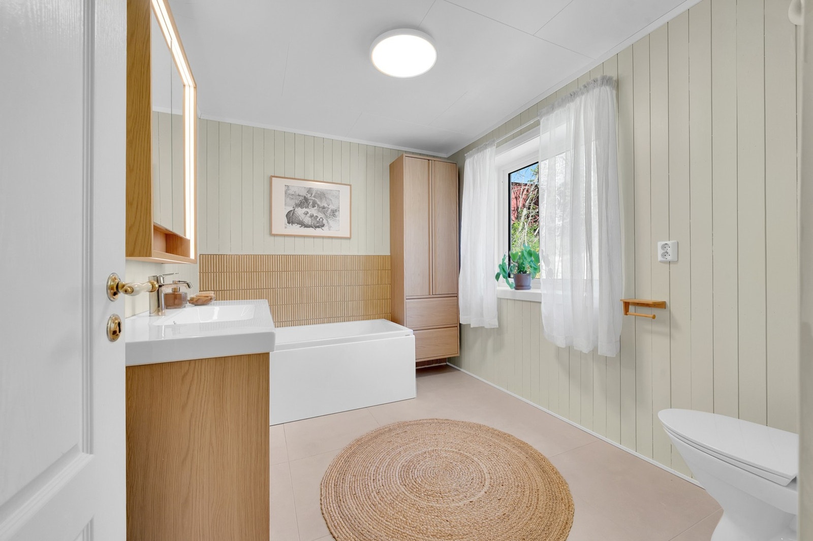 Bad i første etasje med badekar, vegghengt toalett og moderne baderomsinnredning. Galleribilde