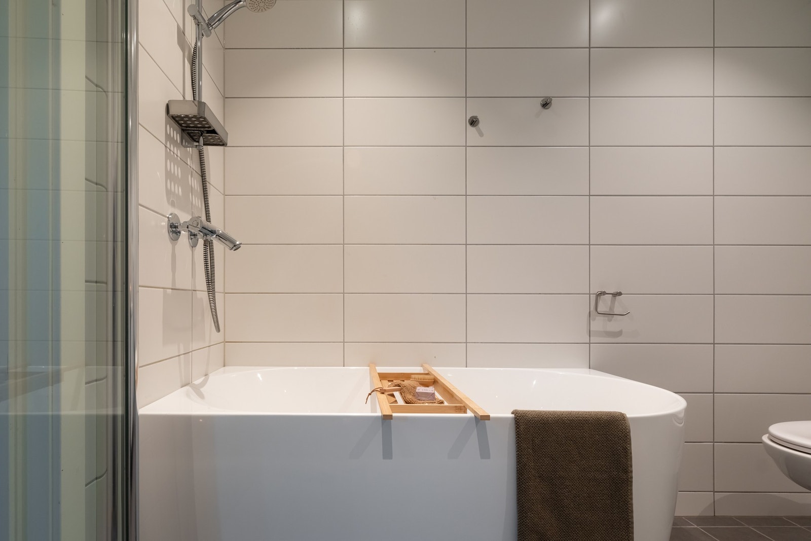 Badet i 1. etasje er lyst og flislagt med downlights i himling og varme i gulv. Innredningen består av servant på underskap, speilskap med lys, vegghengt toalett og badekar. Galleribilde