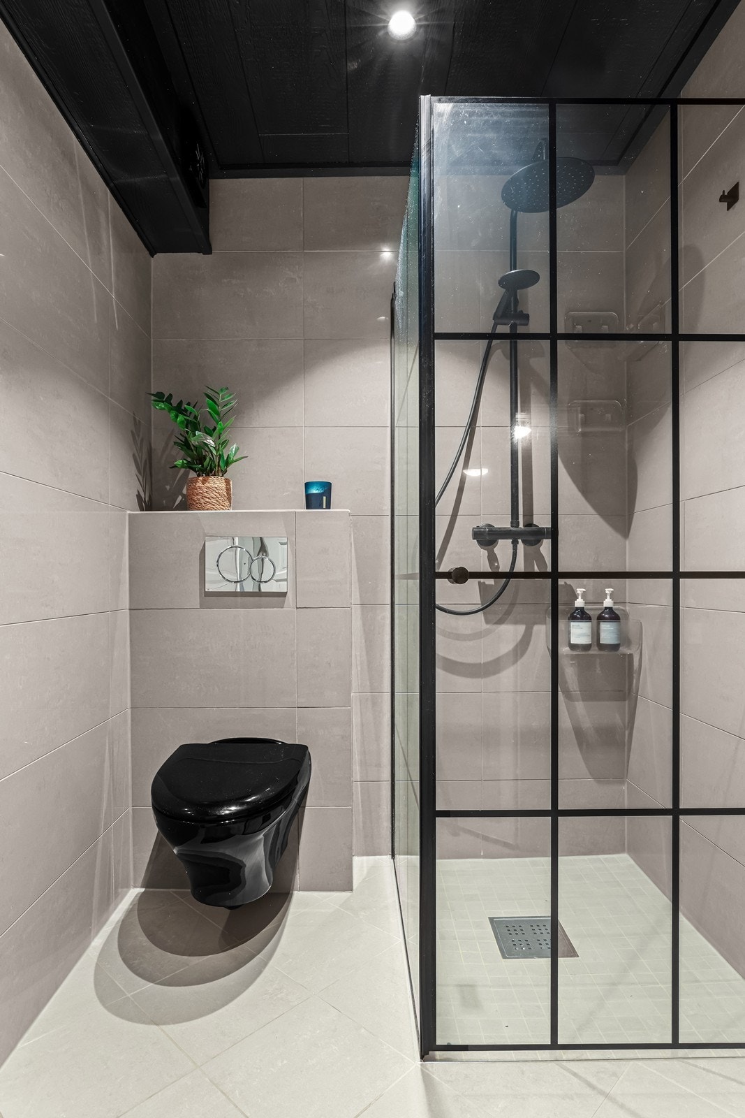 Badet er utstyrt med vegghengt toalett og et dusjhjørne med sorte profiler. Galleribilde