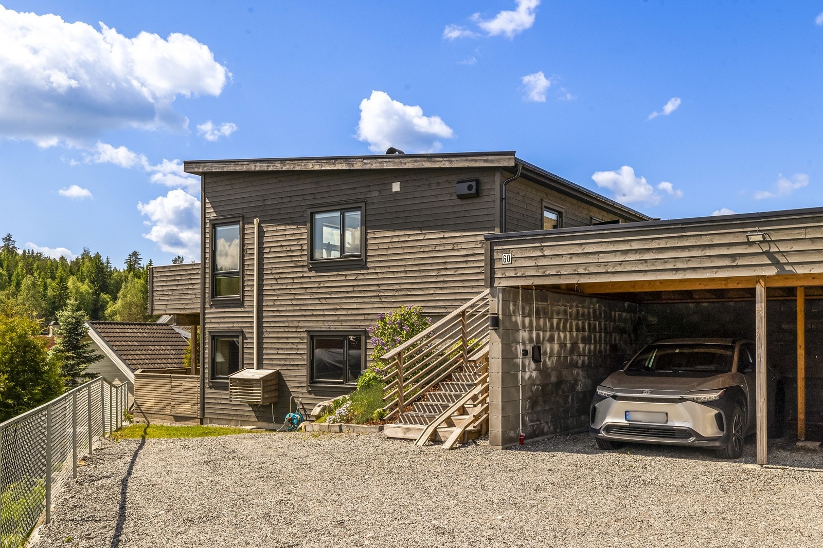 Parkering i carport med elbillader og på felles gruset gårdsplass. Trapp fører opp til inngangsparti. Galleribilde