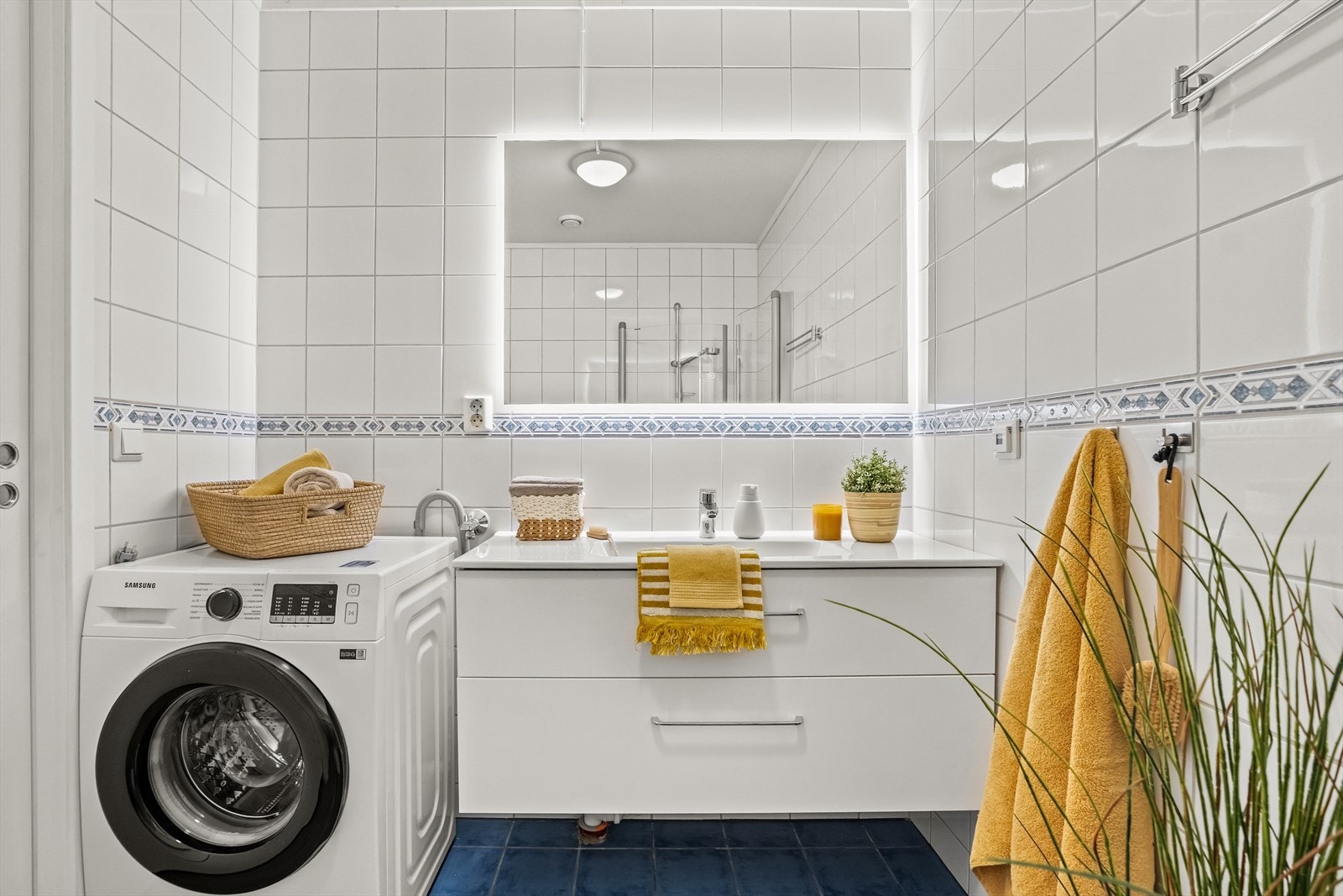 Badet har stor servantinnredning, vegghengt toalett, dusjhørne og opplegg til vaskemaskin Galleribilde