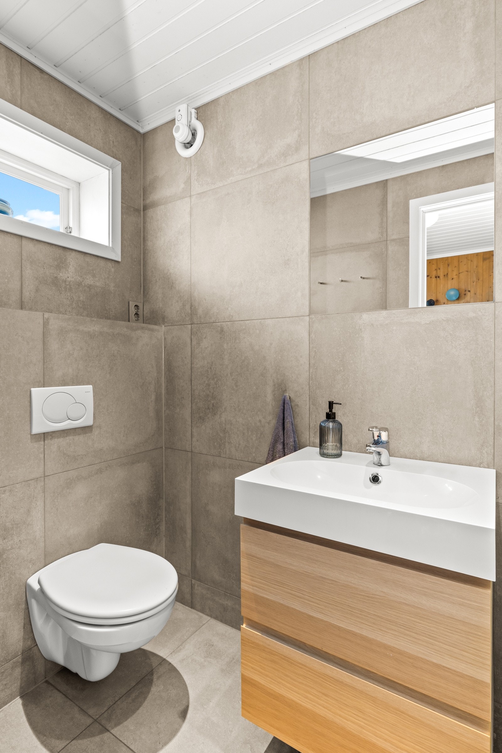 Badet har et stilrent uttrykk med store fliser, lyse overflater og naturlig lys fra vindu. Galleribilde