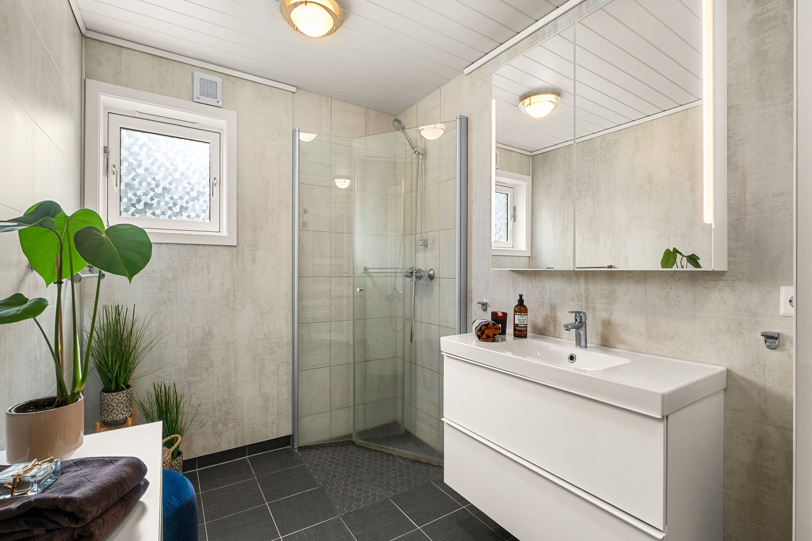 Badet er innredet med servantinnredning, speilskap med integrert lys, veggskap, gulvmontert klosett, åpen dusjløsning med innfellbare dusjdører. Galleribilde