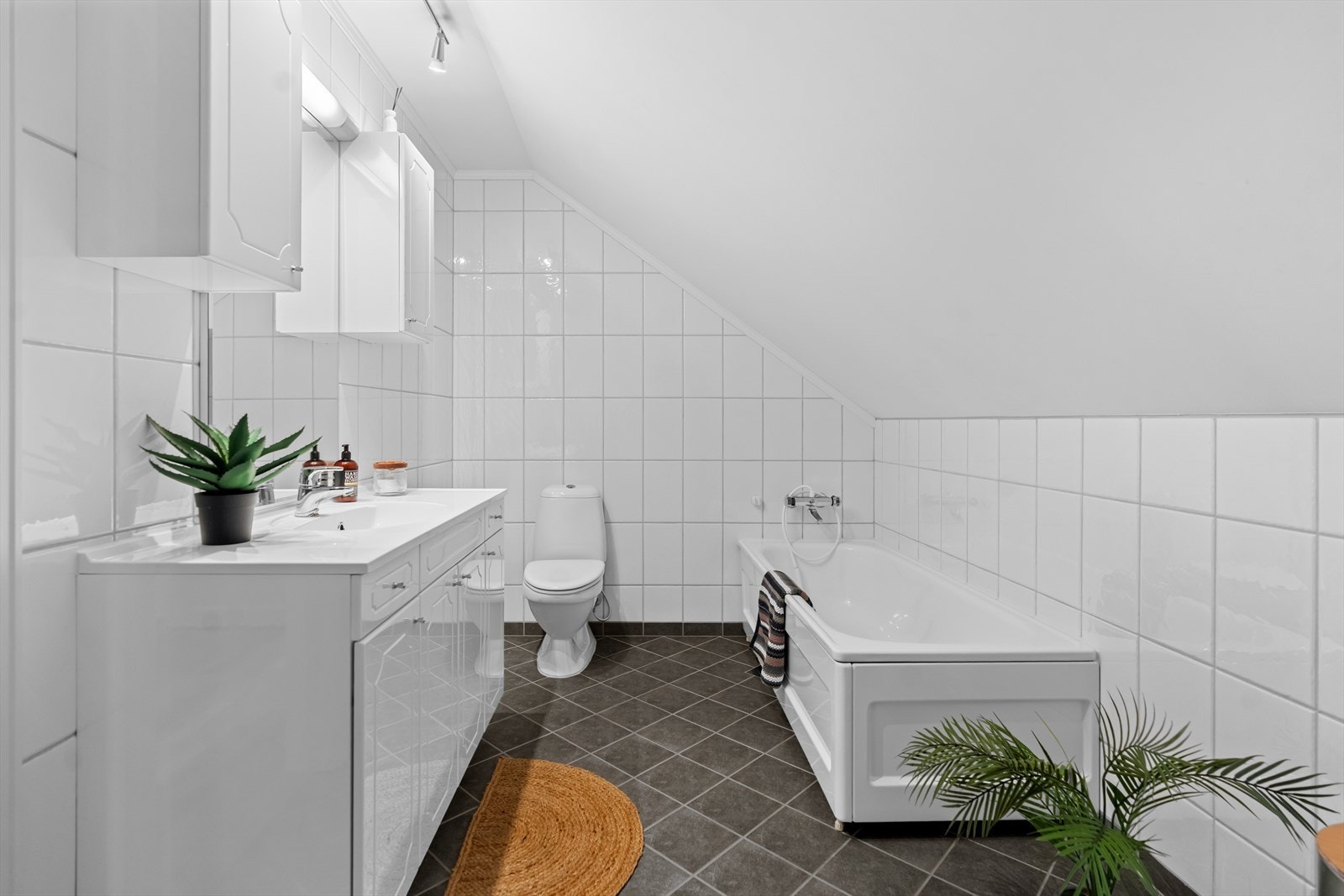 Også badet i 2. etasje har flislagte vegger og gulv. Baderommet er utstyrt med en romslig baderomsinnredning med hvite, profilerte fronter. Innredningen består av et bredt servantskap
med glatte skuffer og skapdører, heldekkende hvit servant og tilhørende Galleribilde