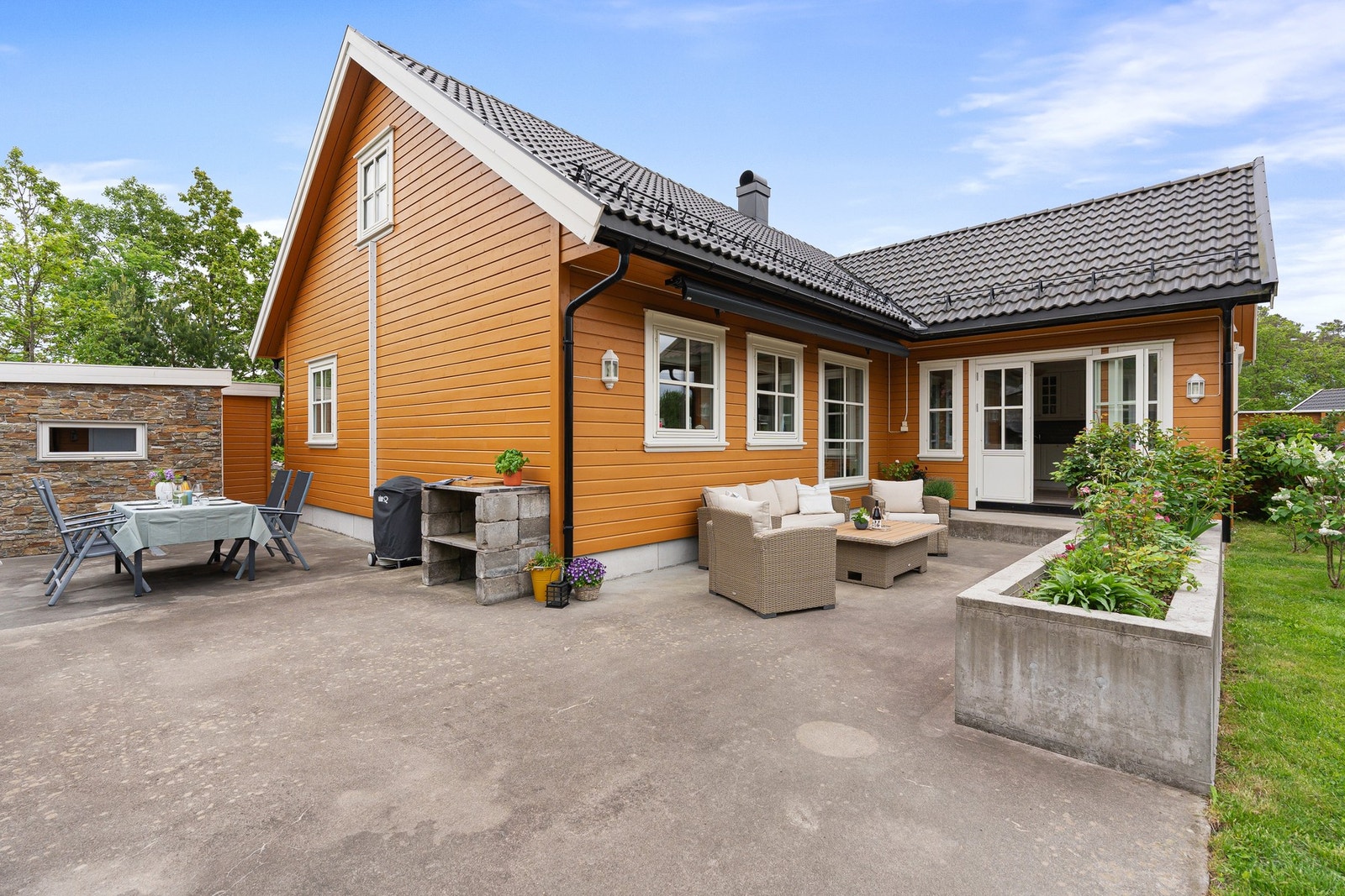 Et vedlikeholdsvennlig støpt dekke og plasstøpt anretning for blomsterbed, skaper et uterom tilrettelagt for hygge og velvære for store og små. Galleribilde