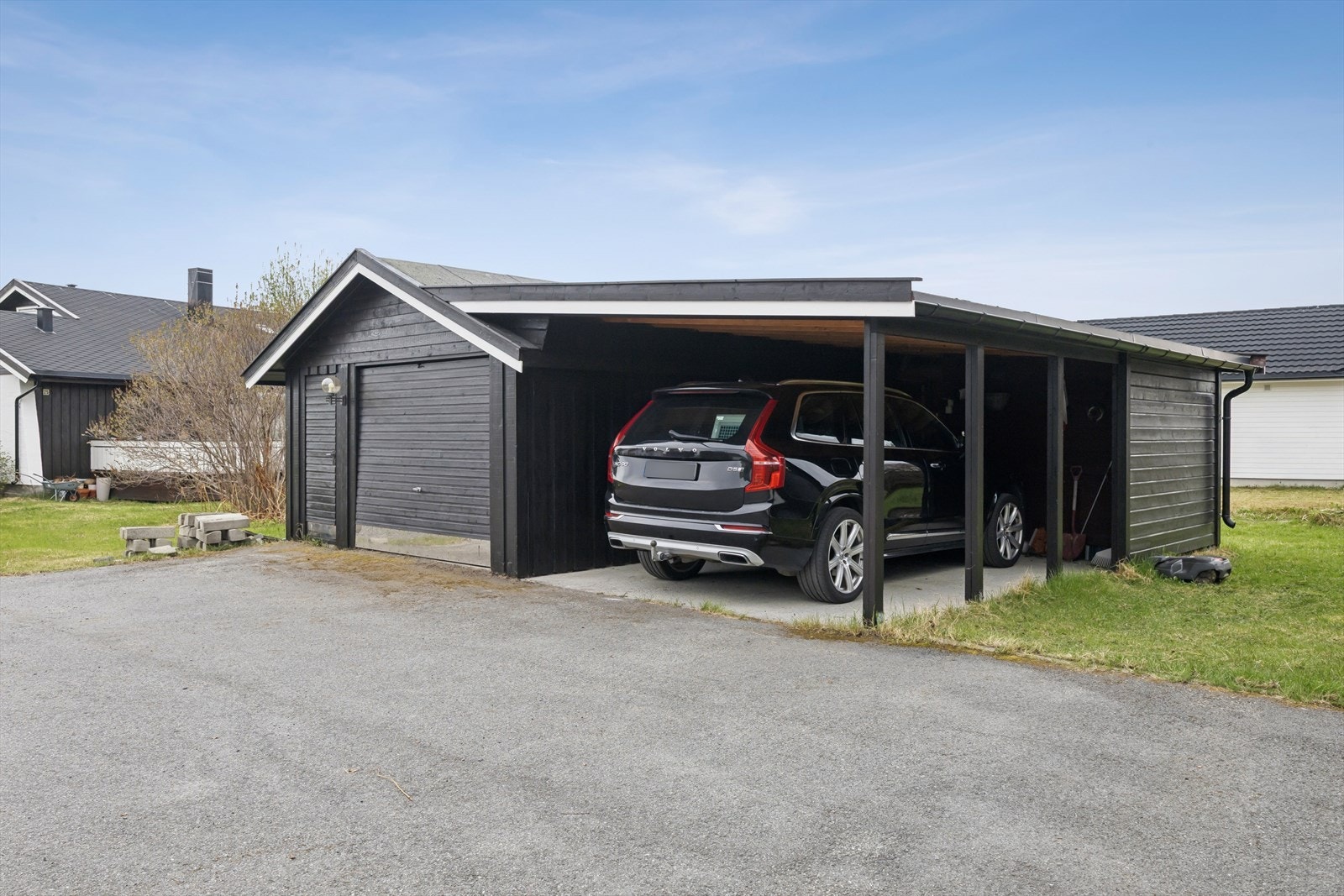 Asfaltert innkjørsel fører til garasje og carport. Galleribilde