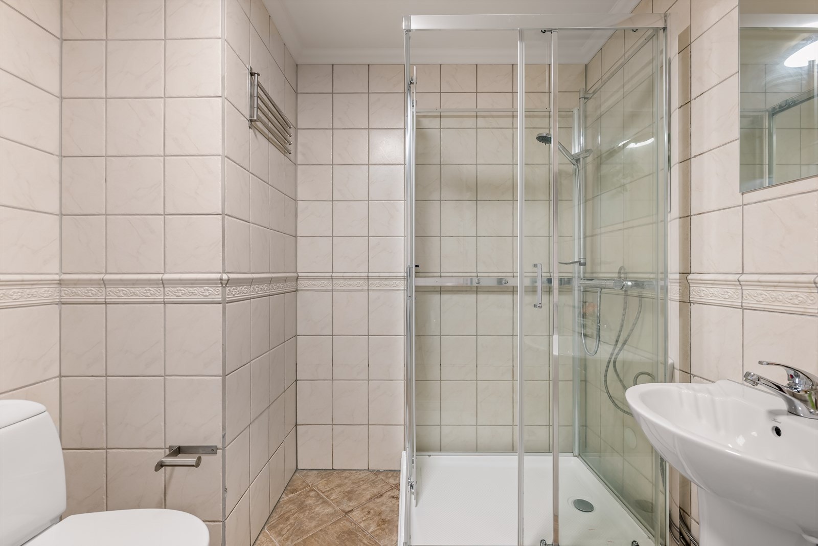 Pent bad med flislagt gulv og vegger. Badet har dusjkabinett, servant og toalett. Galleribilde