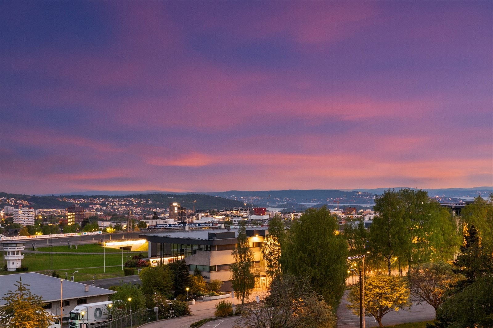 Solnedgangen farger himmelen over byen og fjorden i det fjerne. Galleribilde