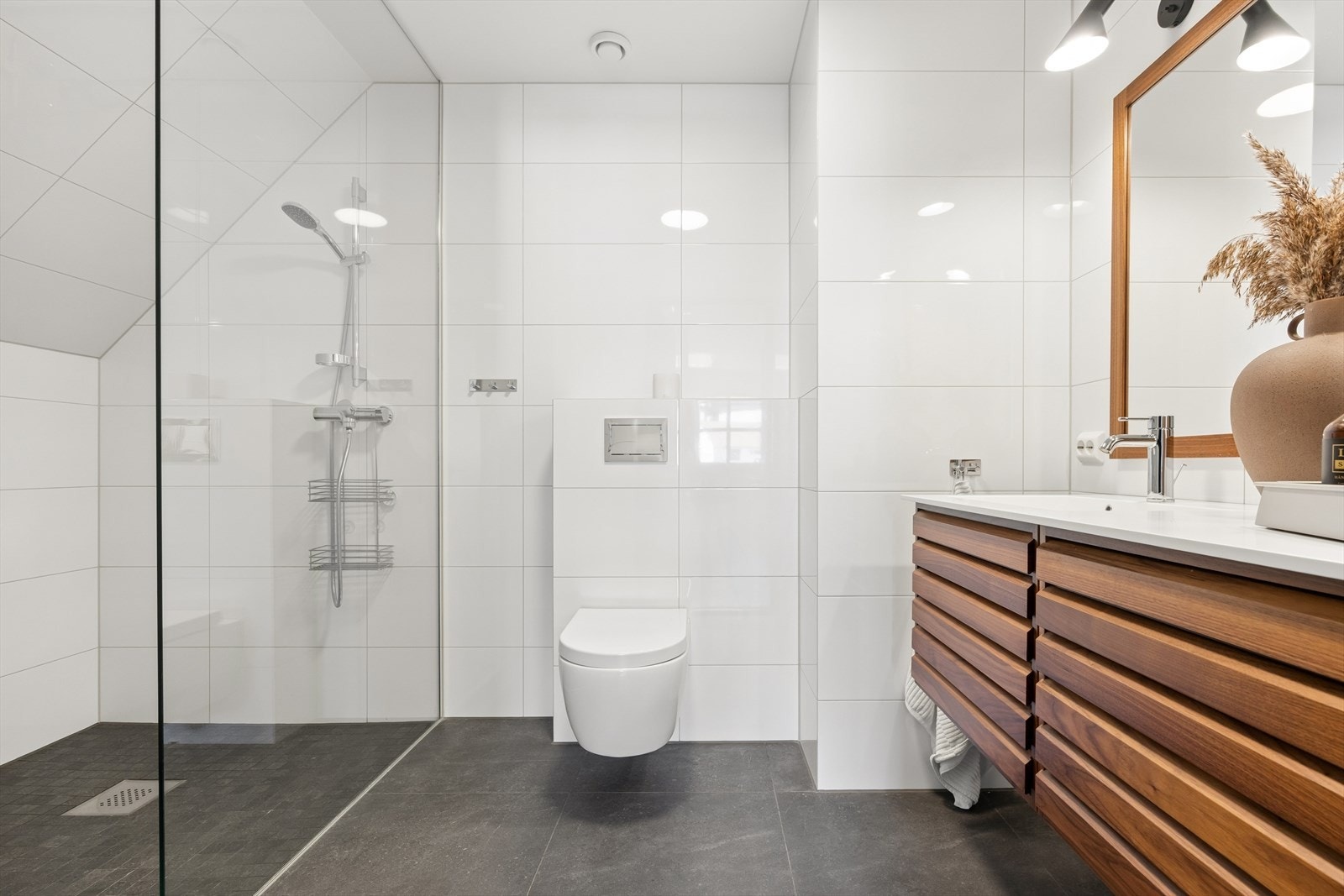 Badet i forbindelse med hovedsoverommet er flislagt med moderne store fliser, har vegghengt toalett, dusjhjørne og servantskap med skuffer Galleribilde