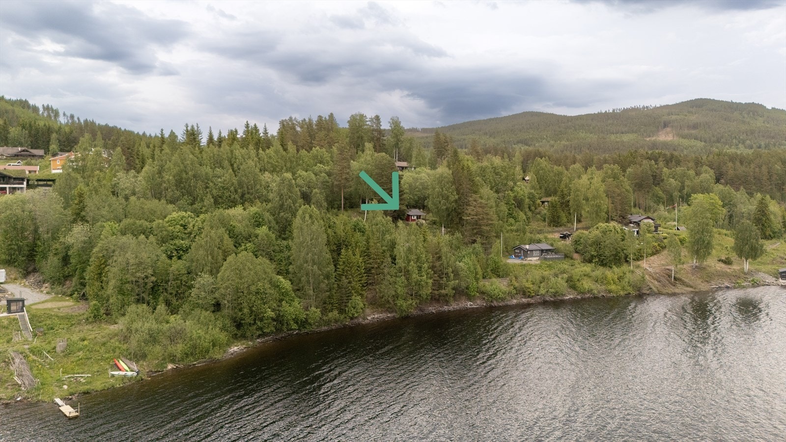 Dronebilde fra Randsfjorden mot hytta og åsene bak der det skjuler seg mer enn bare skog - kontakt megler for mer informasjon! Galleribilde