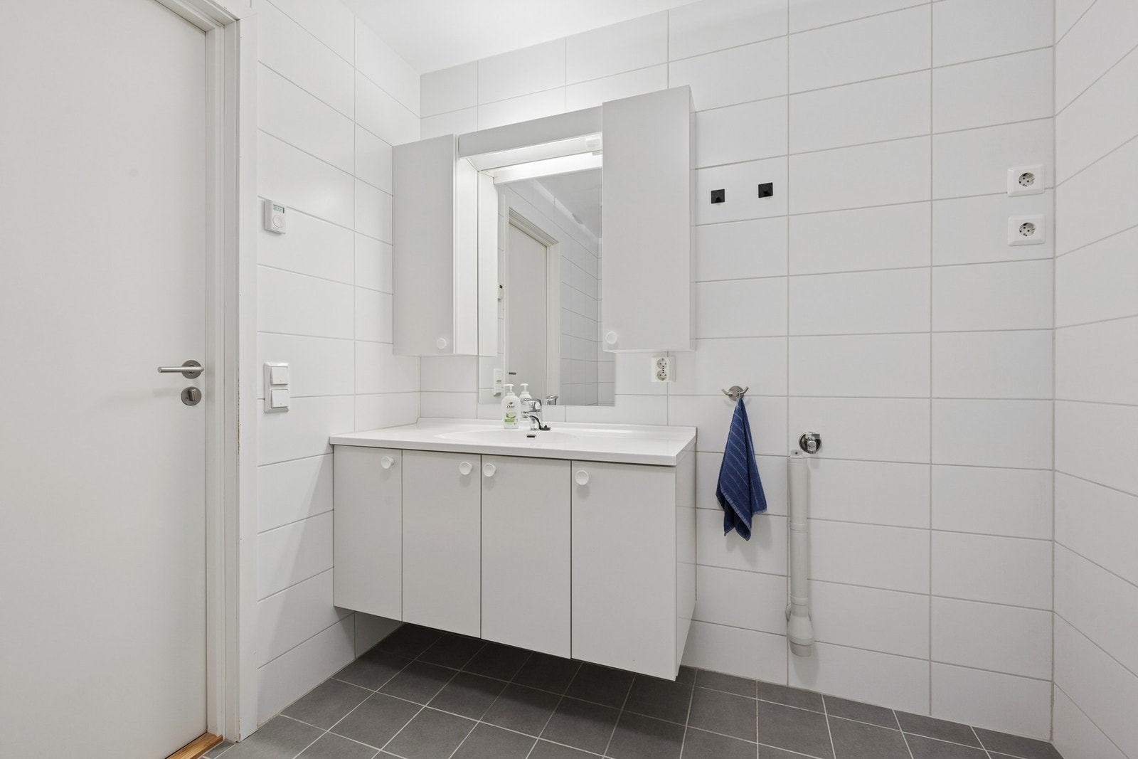 Flislagt bad med servantinnredning, speilskap og opplegg for vaskemaskin. Galleribilde
