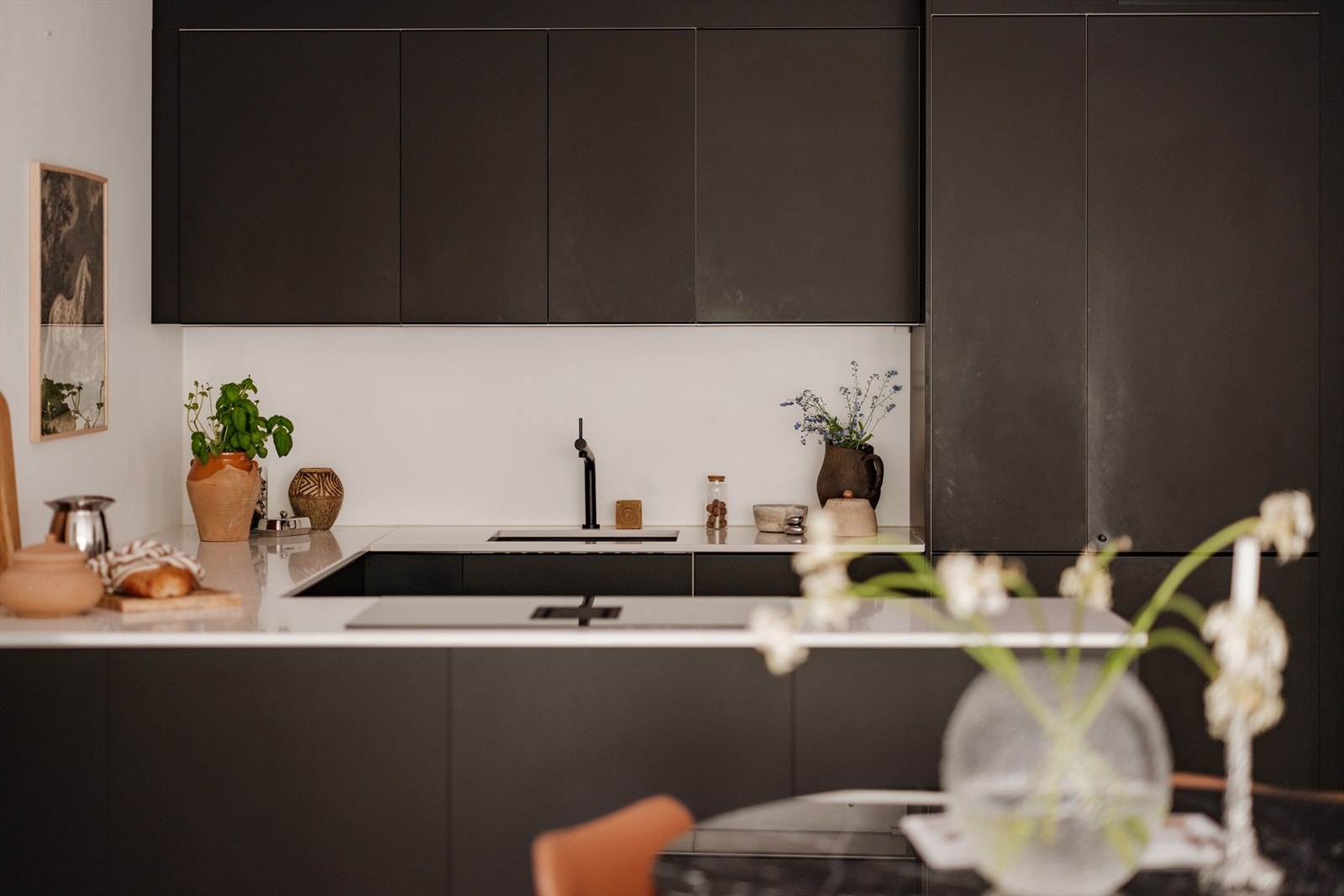 Moderne kjøkken fra IKEA - Innredningen har sort, matte fronter, benkeplate i kompositt, underlimt vask og kullfilterventilator nedfelt i koketopp. Integrerte hvitevarer som stekeovn, oppvaskmaskin og kjøl-/frys. Galleribilde