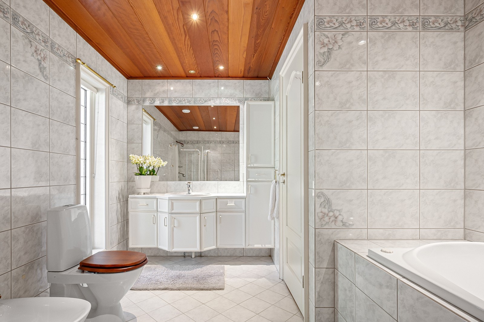 Badet er romslig utformet og skiller seg ut med en særegen kombinasjon av lyse, flislagte overflater og himling i redwood med innfelte downlights. Galleribilde