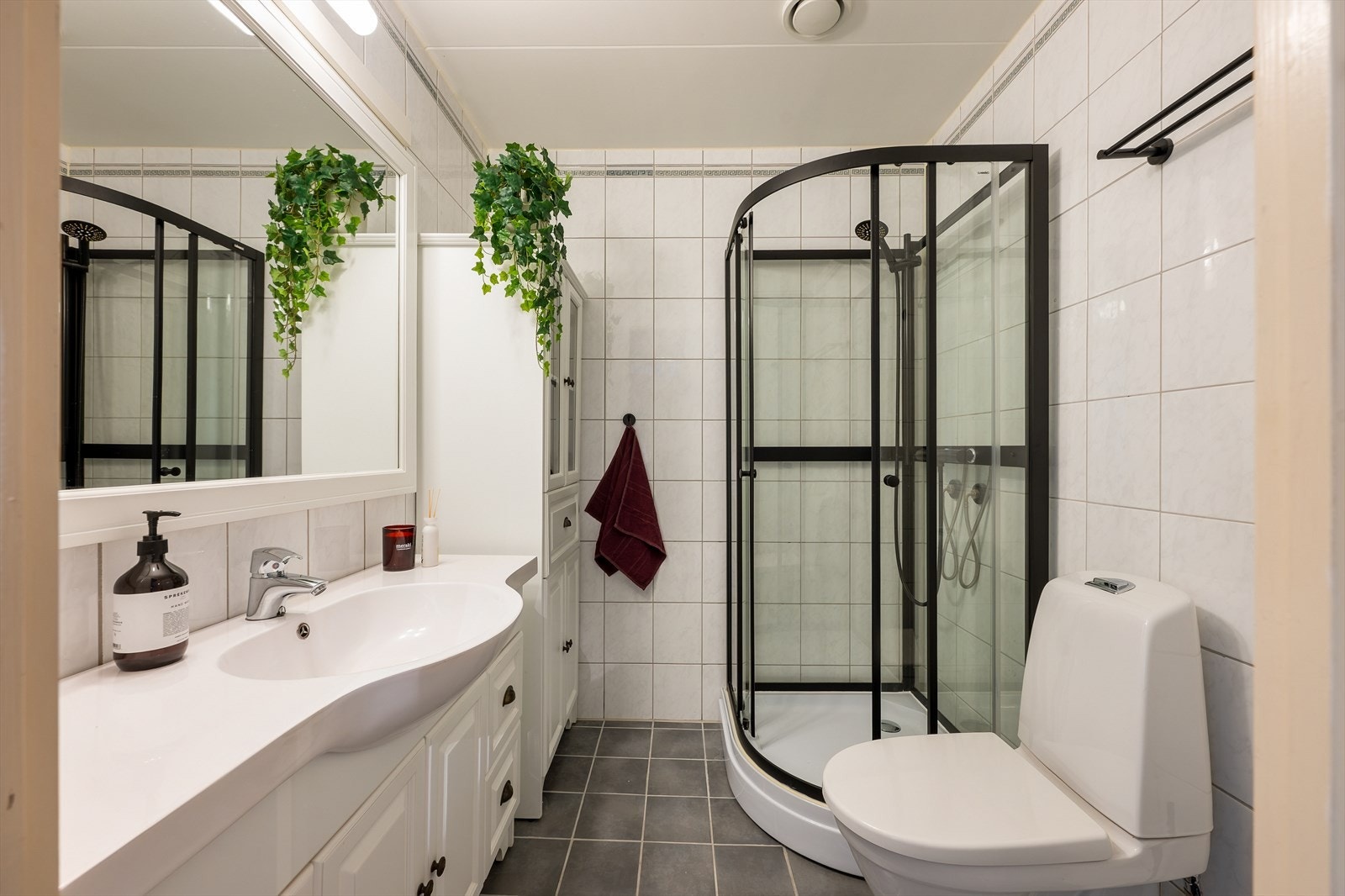 Badet er flislagt med varmekabler i gulvet. Rommet er utstyrt med toalett, dusjbakinett, opplegg for vaskemaskin og en innredning med heldekkende servant. Galleribilde