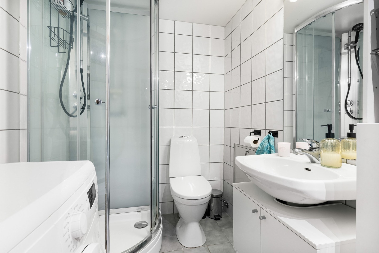 Badet i leiligheten fremstår som velholdt og pent, med hvite fliser på veggene og lyse fliser på gulv med gulvvarme. Galleribilde