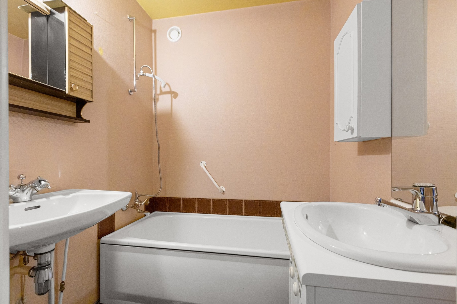 Bad med to servanter og badekar med dusjløsning. Gulvet har malte fliser. Badet har behov for totalrenovering. Galleribilde