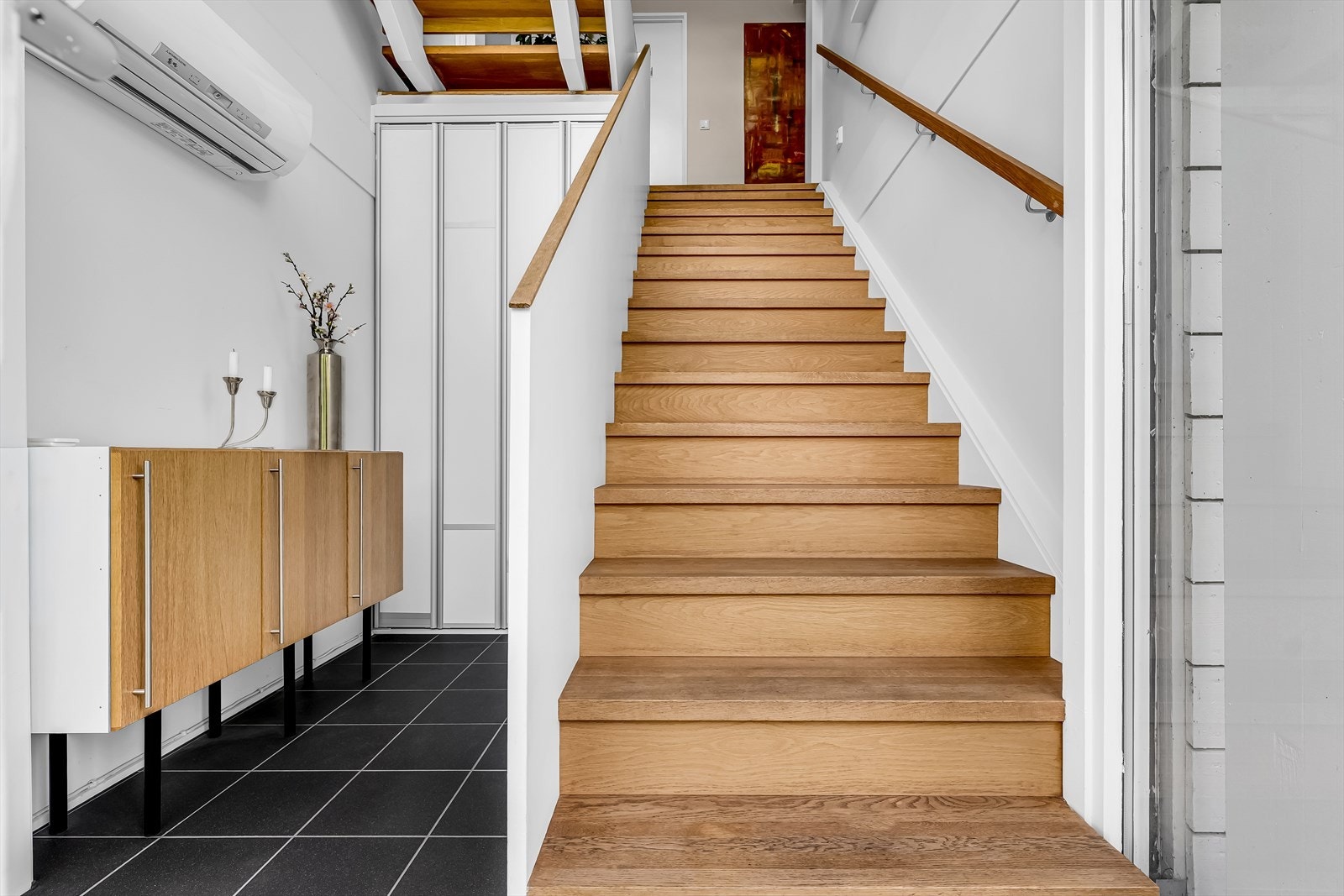Flott eike trapp ned til underetasjen fra hoveddelen. Her har man praktisk oppbevaringsløsning under trapp, samt mulighet for åpning inn til hybeldel. Direkte utgang til solrik hage. Galleribilde