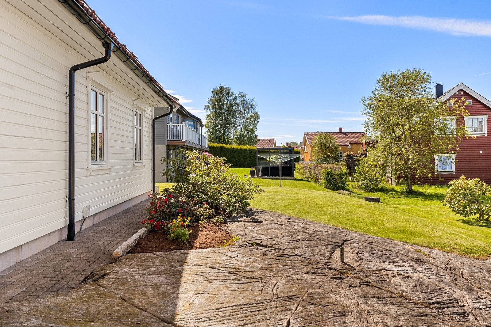 Tomten er relativt flat med noe fjellknauser og naturterreng opparbeidet med grønn plen, hekk, bed og granitt kantstein. Galleribilde
