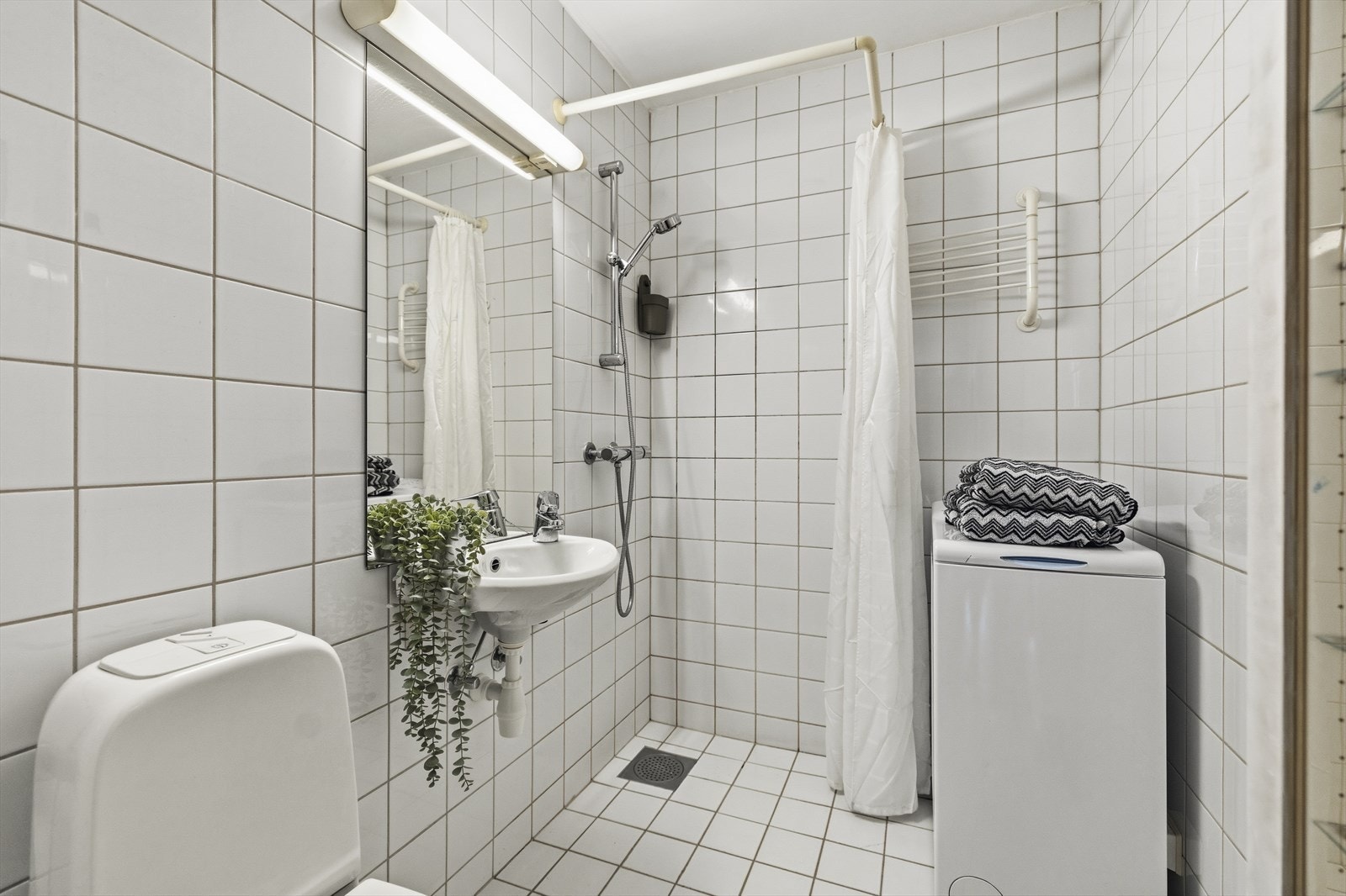Flislagt bad i hybelen med dusj, toalett, servant og opplegg for vaskemaskin. Galleribilde