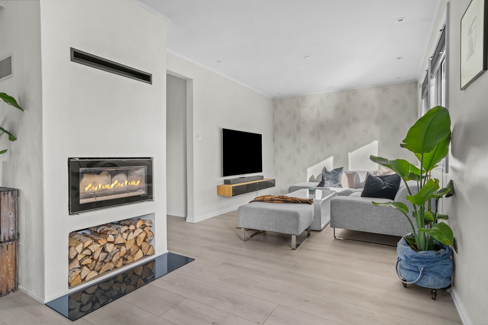 Stuen er innredet med gasspeis og egen TV-sone. Lys tapet, downlights og gjennomgående gulv bidrar til et helhetlig uttrykk. Galleribilde