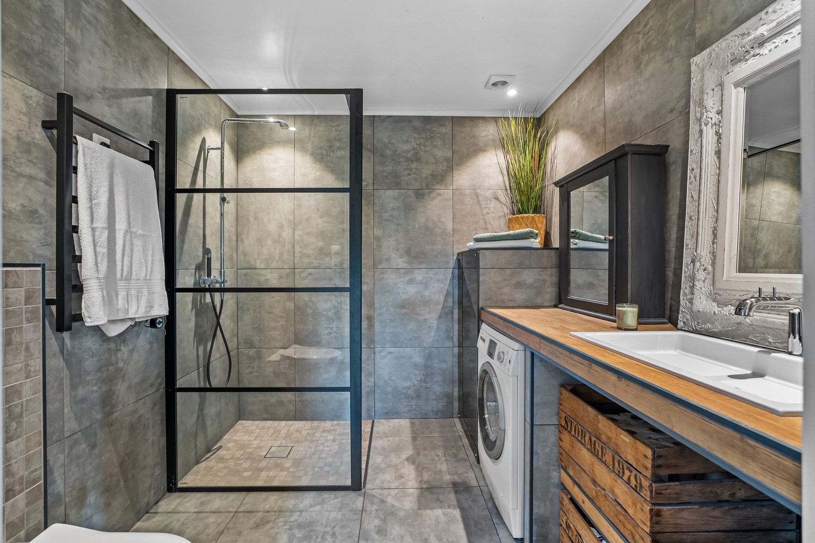 Badet er innredet med store fliser i grå utførelse og dusjsone med sorte profilerte glassvegger. Heldekkende benkeplate i tre tilfører varme til rommet og står i fin kontrast til flisene. Galleribilde