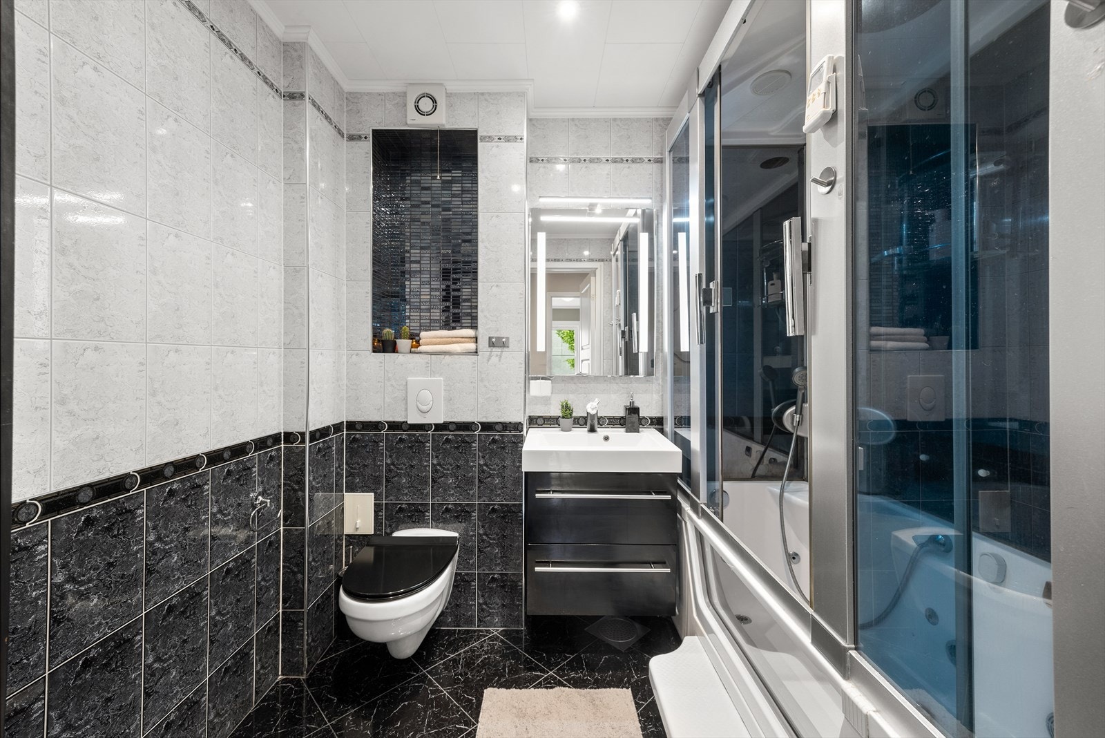 Badet er innredet med servantskap med ett-greps blandebatteri, veggspeil med speilbelysning, veggengt toalett med innebygget sisterne og dusjkabinett. Det er avtrekk via elektrisk styrt baderomsvifte. Galleribilde