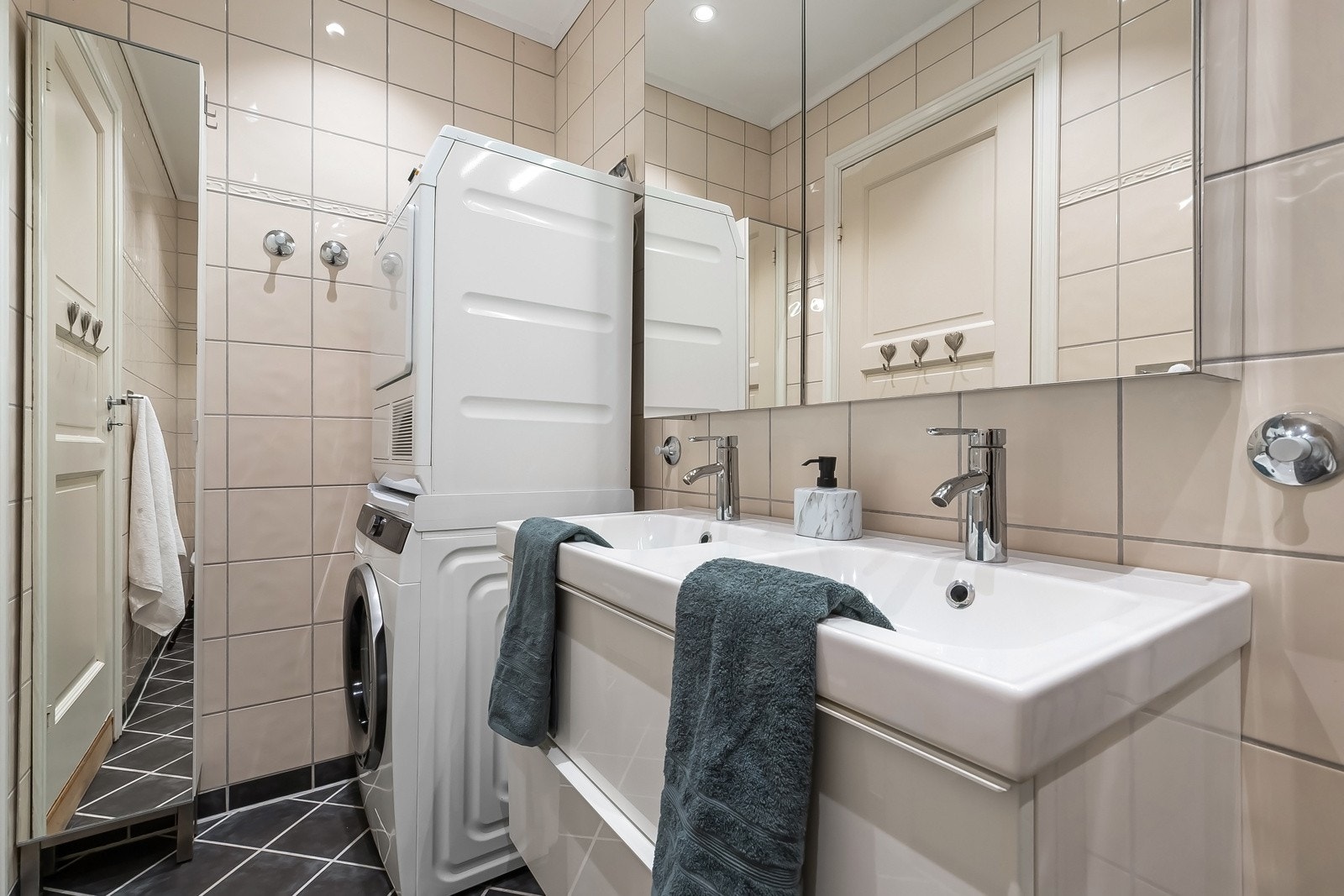 Badet er flislagt med gulvvarme og har en tidløs utførelse med dusjhjørne i glass, heldekkende dobbel servant, speilskap med belysning og opplegg for vaskemaskin og tørketrommel. Galleribilde