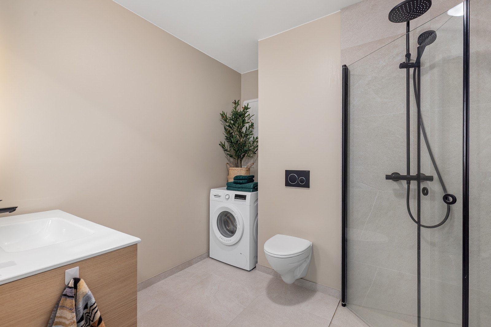 Badet fremstår moderne og funksjonelt, med flislagt gulv og fliser på veggene i dusjsonen. Materialvalgene gir et stilrent uttrykk og en praktisk løsning som er enkel å vedlikeholde. Galleribilde