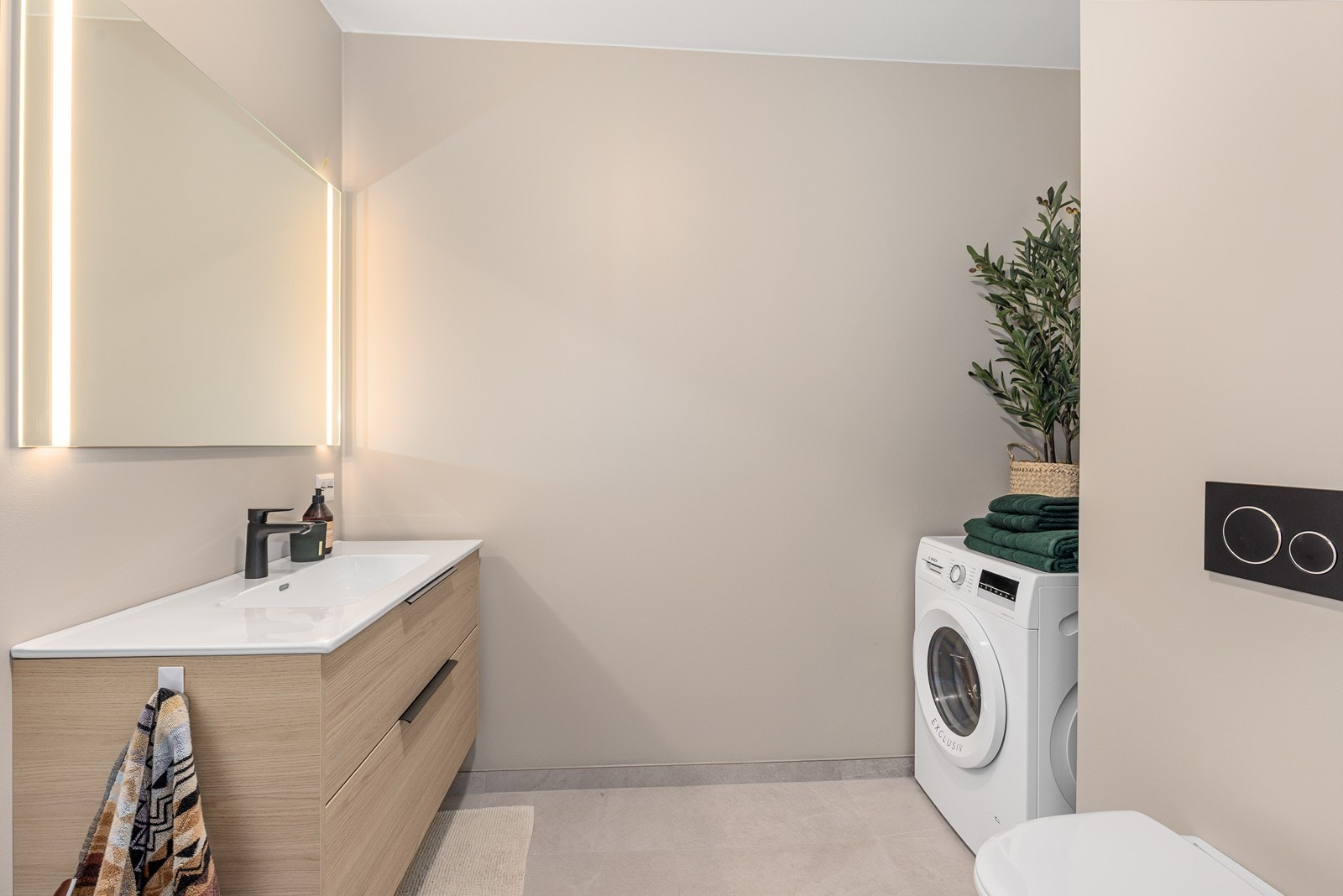 Badet er innredet med vegghengt toalett med innebygget sisterne, servant med nedfelt vask, dusjdører med regnfallsdusj, samt opplegg for vaskemaskin. Løsningen gir et stilrent uttrykk og god brukervennlighet i hverdagen. Galleribilde