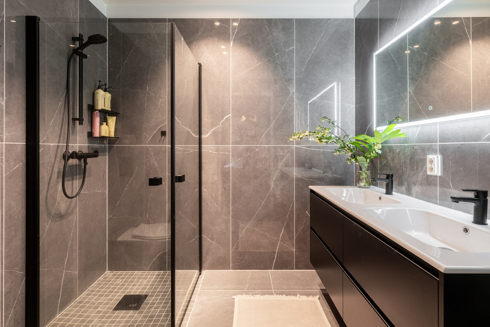 Badet består av moderne baderomsinnredning med heldekkende servant nedfelt i underskap, veggmontert toalett og eget dusjhjørnet med glassdører. Galleribilde