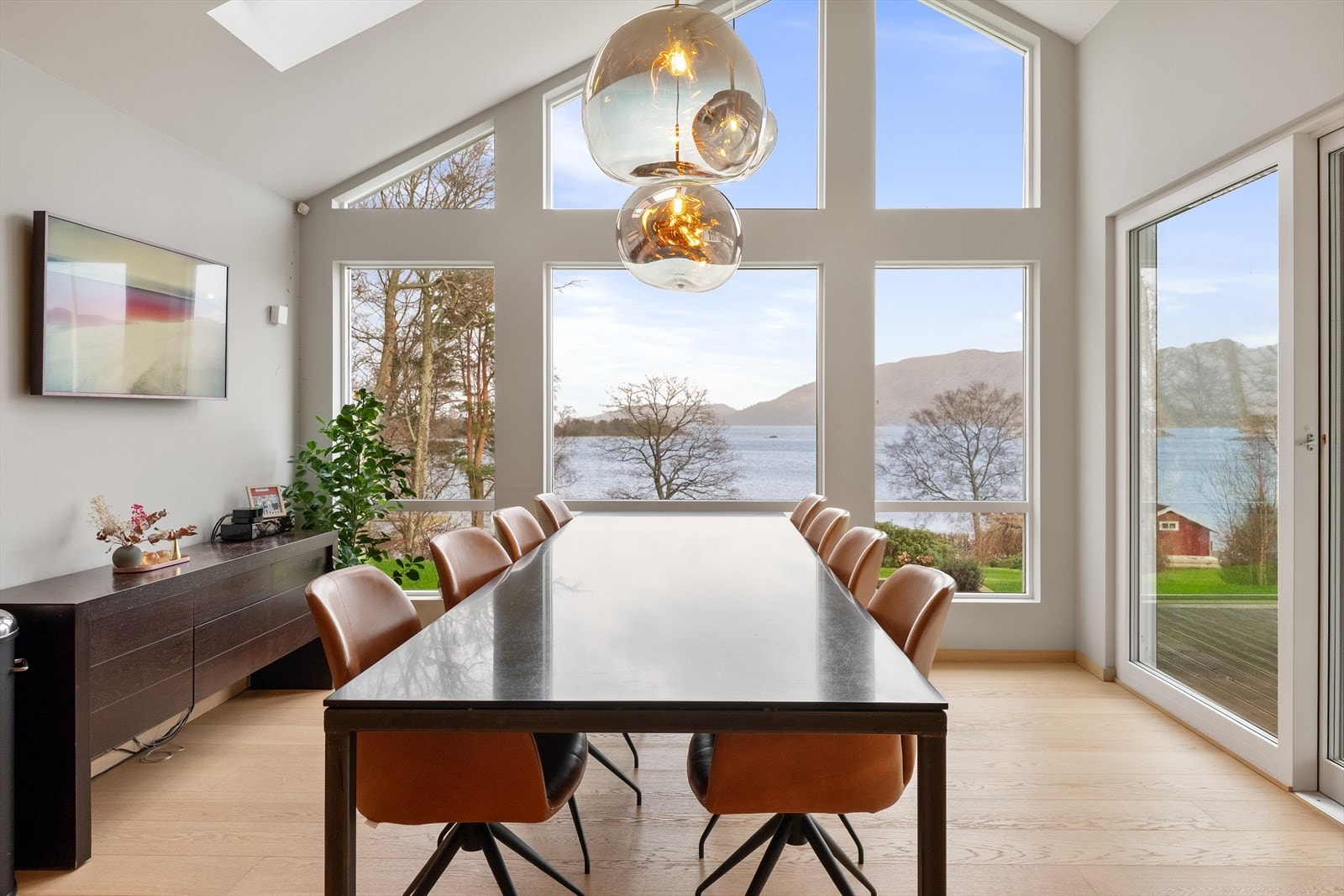Spisestuen har plass til et stort langbord og er rammet inn av vinduer fra gulv til tak. Galleribilde
