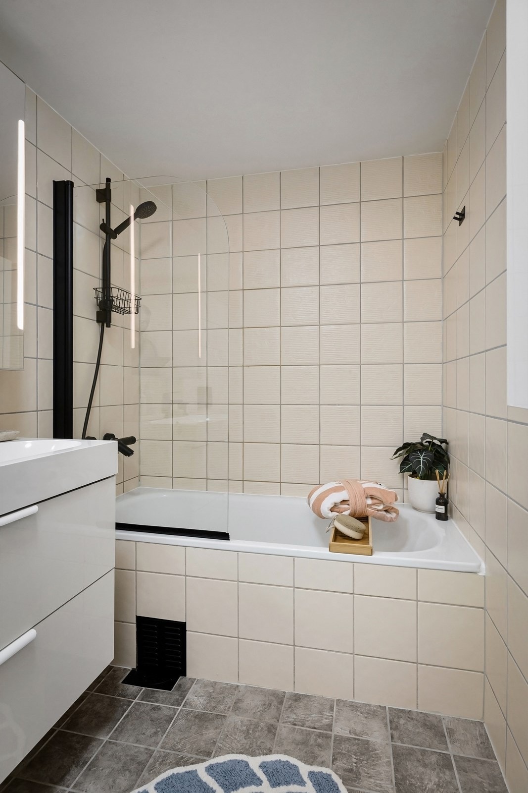 Badet er innredet med vegghengt klosett, servant med innredning, speil med lys og badekar med svingbar glassdør Galleribilde