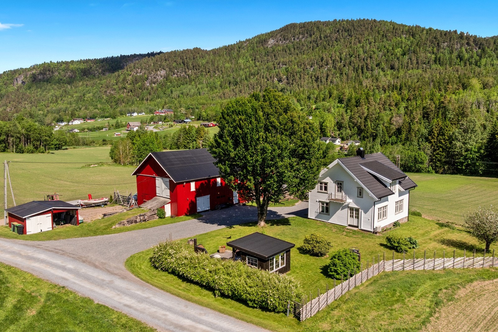Idyllisk tun med tun tre, tradisjonell låve, garasje med carport og "utestue" Galleribilde