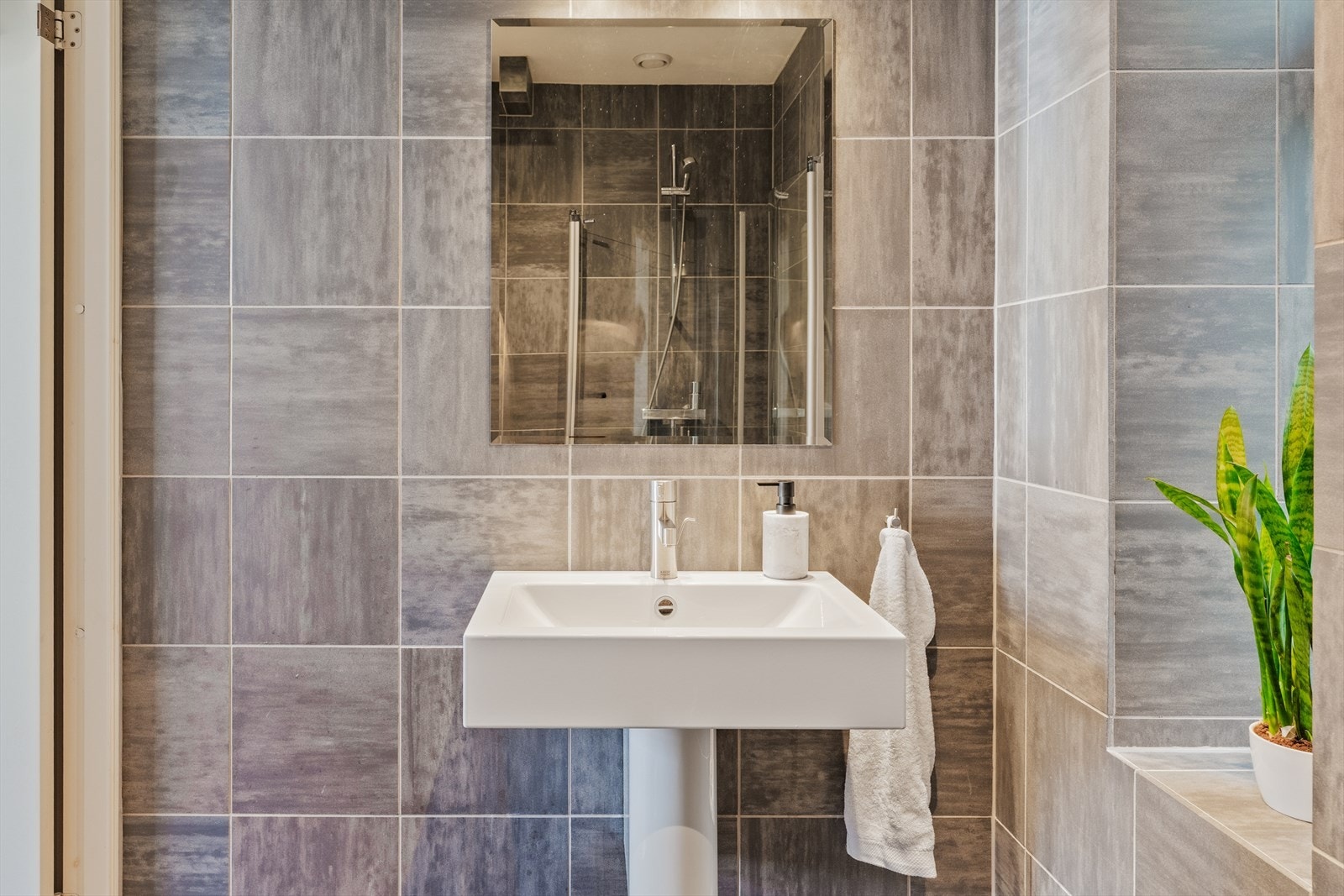 Badet er flislagt og har et moderne og innbydende uttrykk med servant, veggmontert toalett, dusjvegger i glass og varmekabler i gulv. Galleribilde