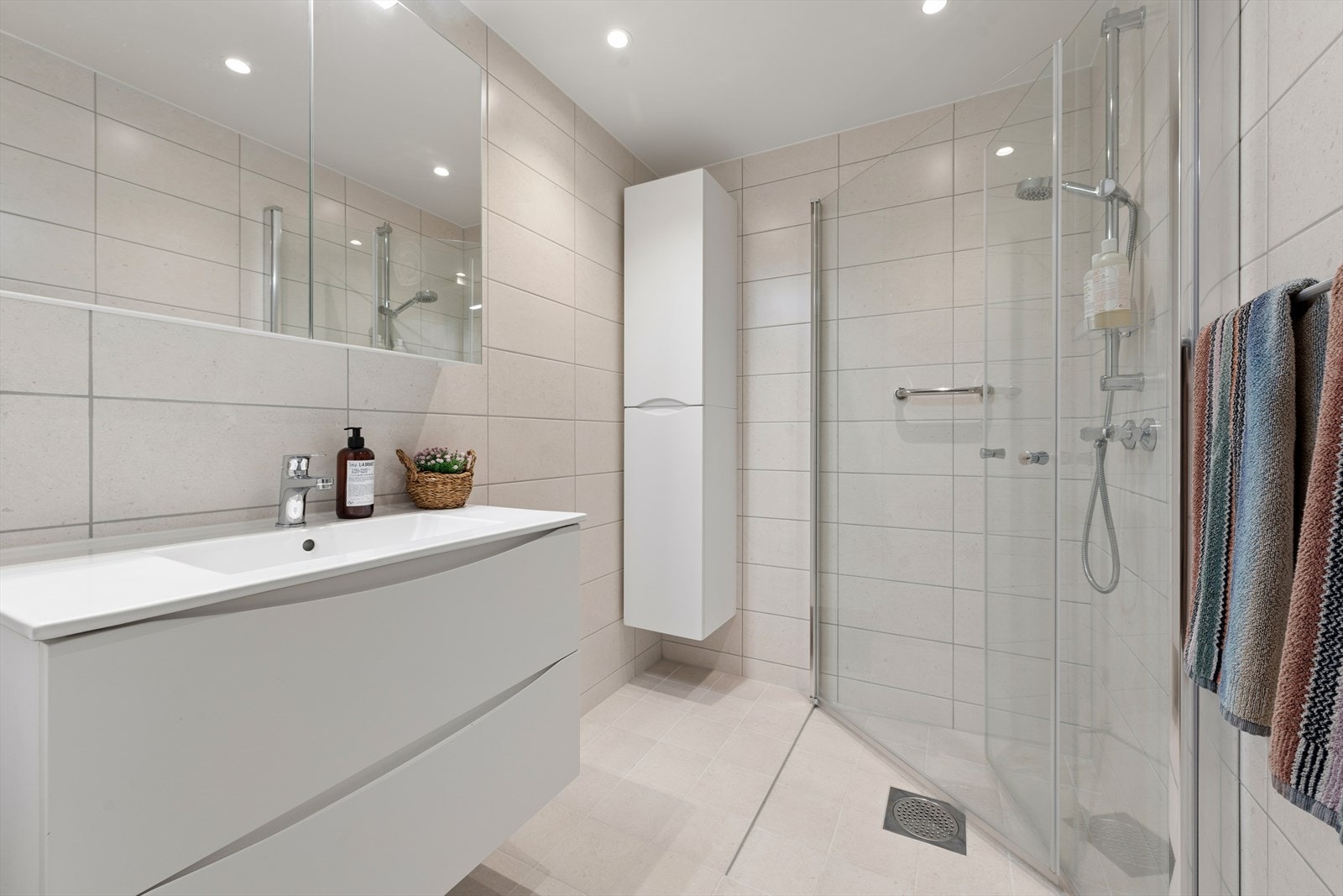 Lekkert og nytt bad fra 2024 med sandfargede fliser på gulv og vegger, med underliggende varme i gulv. Badet er videre utstyrt med heldekkende servant, speilskap, høyskap og dusj m/innfellbare glassdører, samt downlights i himling Galleribilde