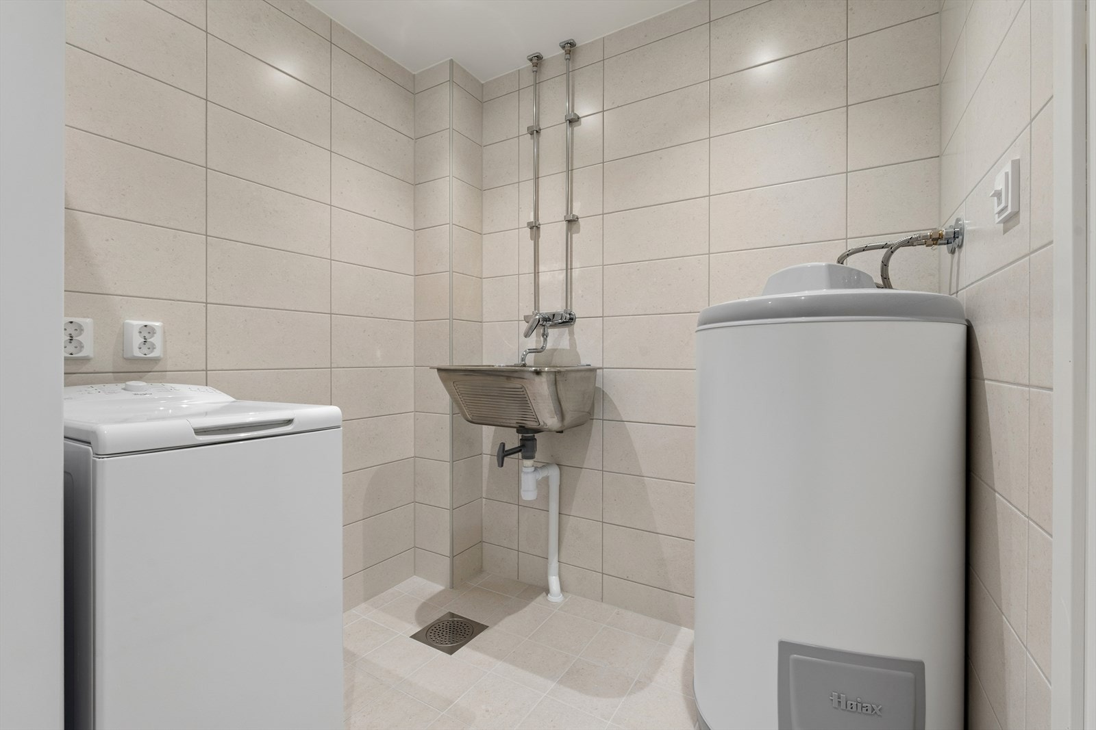 Praktisk vaskerom som ble rehabilitert i 2025. Vaskerommet er innredet med sandfargede fliser på gulv og vegger, med underliggende varmekabler i gulv. Badet er videre utstyrt med utslagsvask, opplegg for vaskemaskin/tørketrommel og varmtvannstank Galleribilde