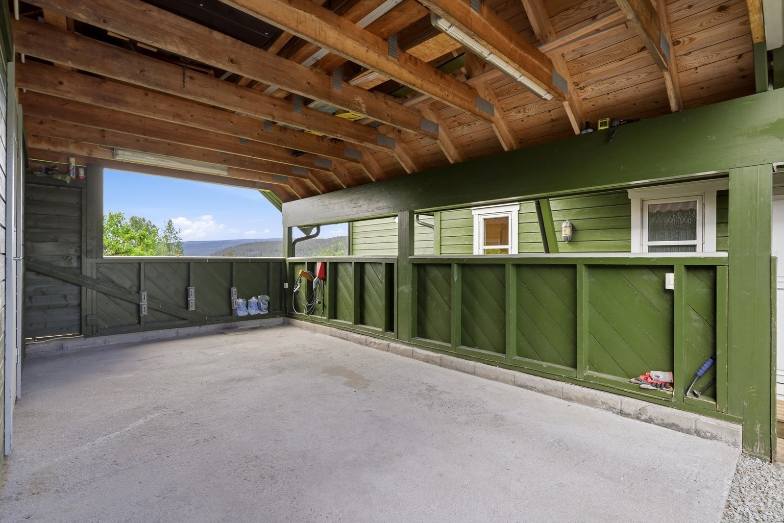 Carport som egentlig er dobbel, men hvor venstre del har blitt innredet som boddel i nyere tid. Elbillader er montert på vegg til høyre Galleribilde