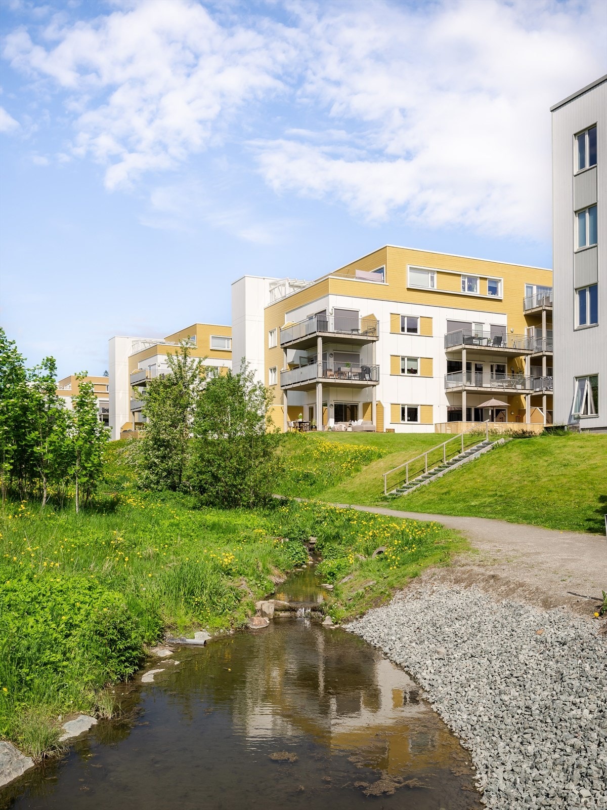 Mellom blokkene er det etablert fine, beplantede fellesareal med sosiale møteplasser og lekeplass for barn. Fra leiligheten ser man den koselige bekken og bruen. Galleribilde