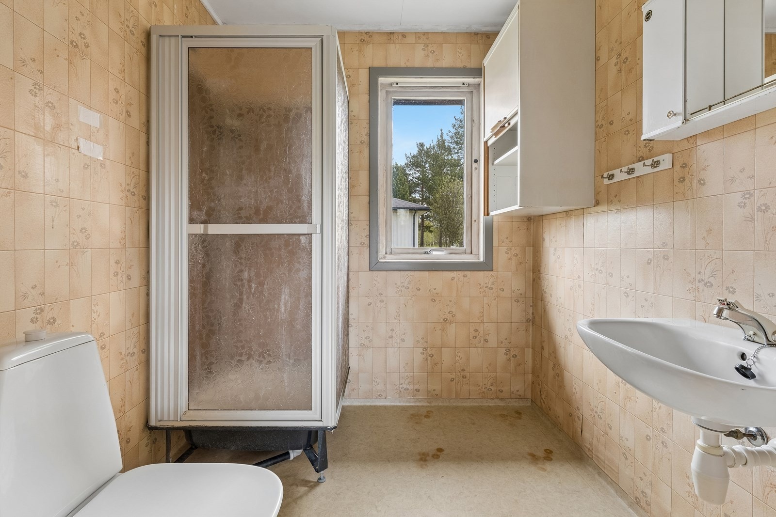Badet er innredet med dusjkabinett, toalett og servant. Overflatene består av våtromsbelegg på gulv og våtromstapet på vegg. Galleribilde