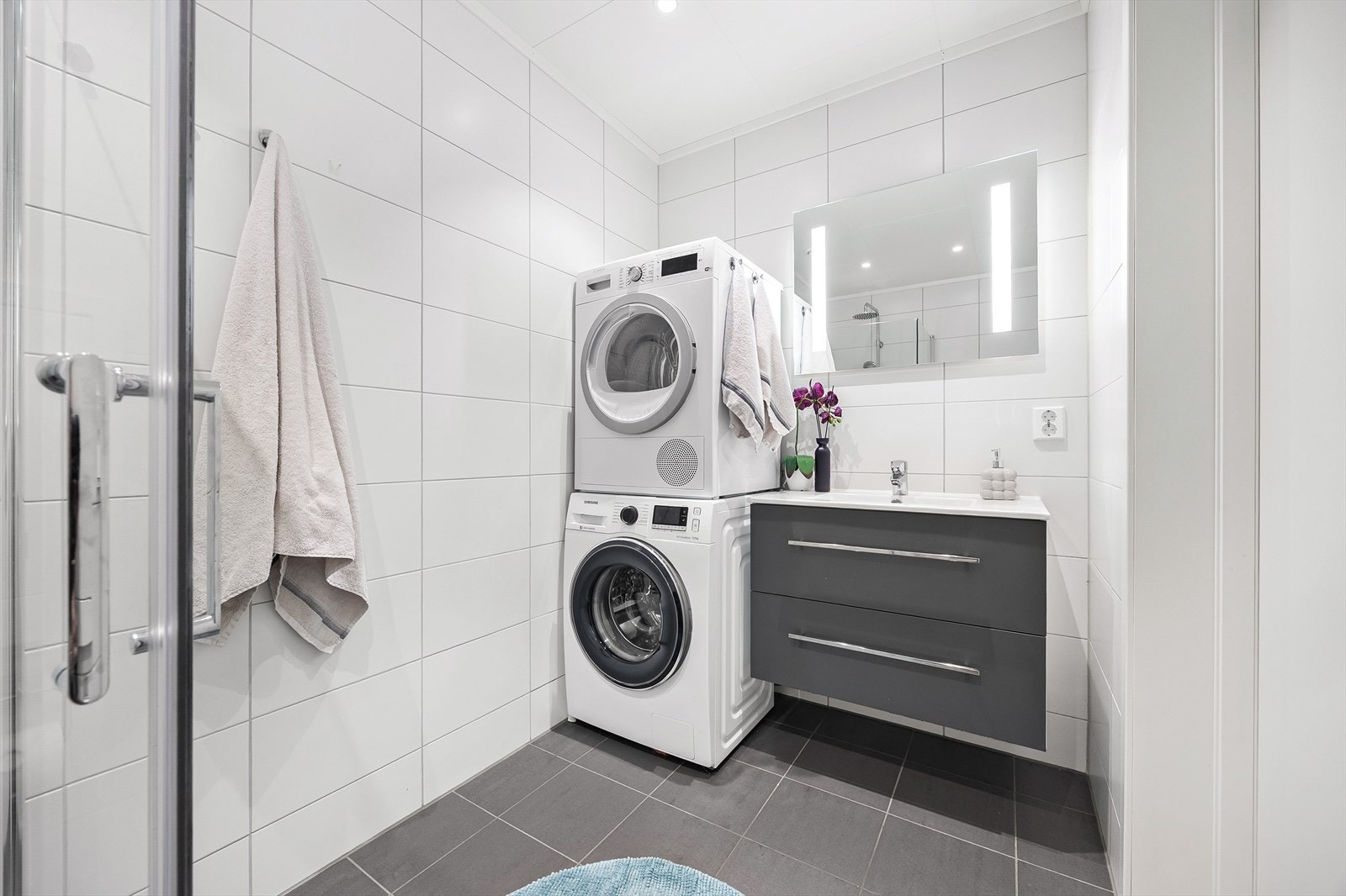Badet er innredet med servant i baderomsinnredning, speil med integrert belysning og opplegg for vaskemaskin og tørketrommel. Galleribilde