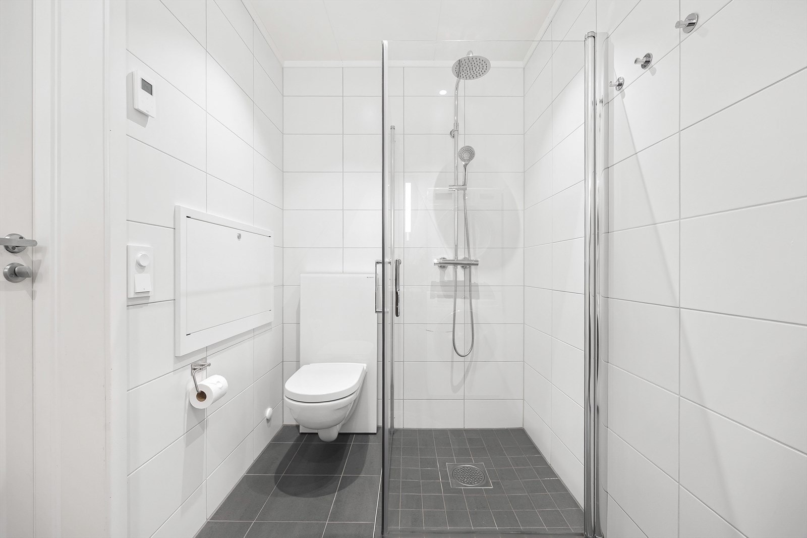 Badet er innredet med vegghengt toalett og dusjhjørne med innfellbare glassvegger. Galleribilde