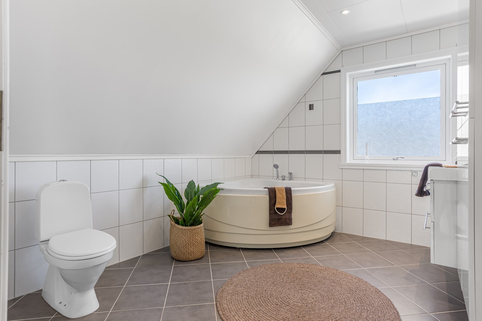 Badet i loftsetasjen har servant, toalett og badekar. Flislagt gulv med elektriske varmekabler. Flis på vegger og takplater i himling. Galleribilde
