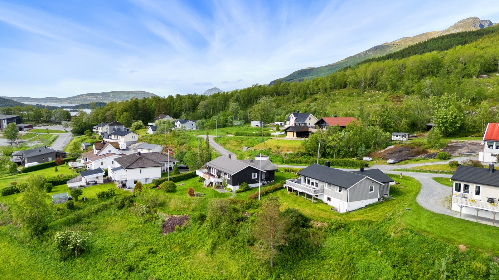 Rolig og etablert boligfelt med eneboliger, grønne tomter og kort avstand til barneskolen. Boligen med mørk kledning er godt synlig midt i bildet Galleribilde
