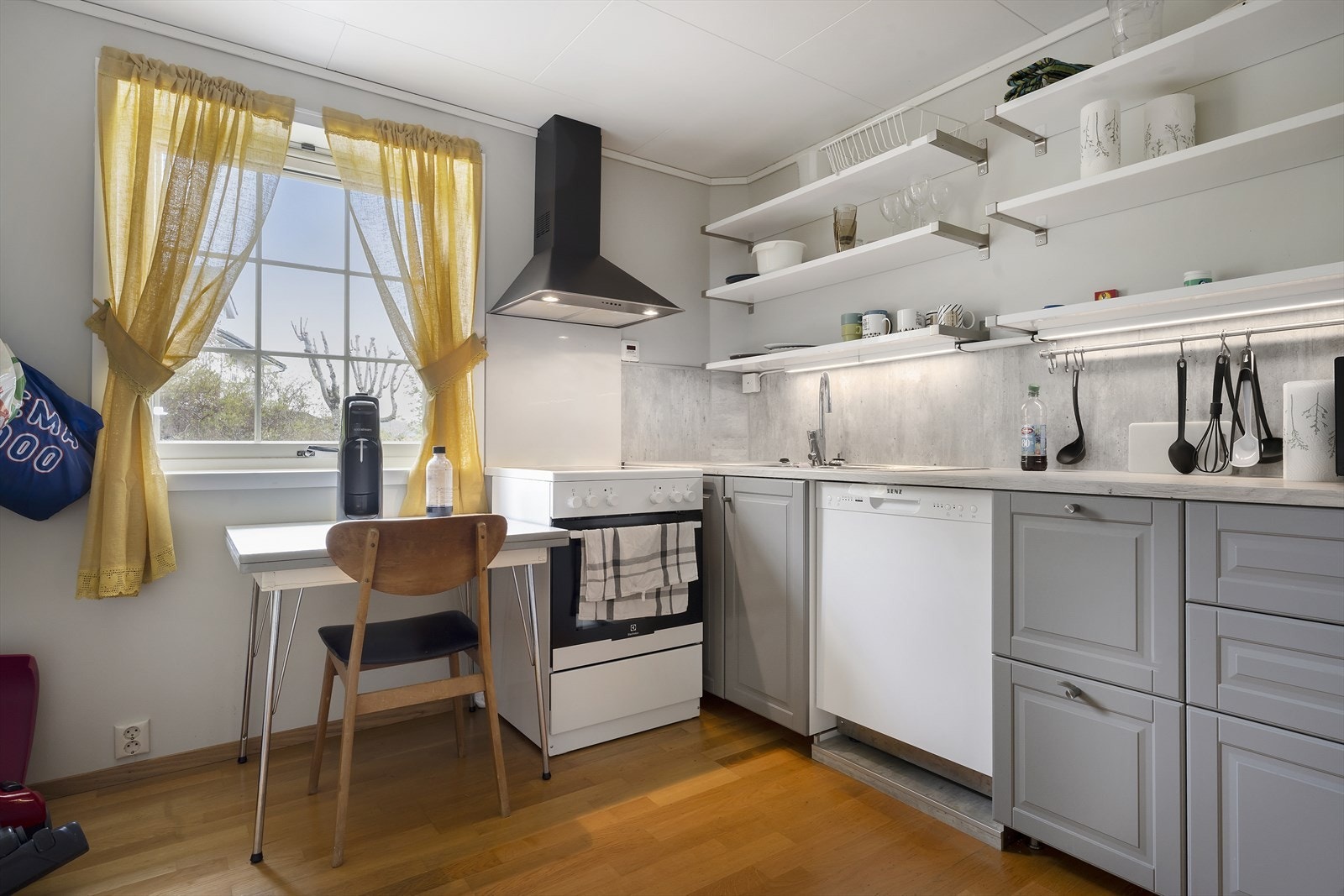 Kjøkkeninnreding med lyse profilerte fronter. Frittstående hvitevarer i form av komfyr, oppvaskmaskin og kjøl/fryseskap. Galleribilde