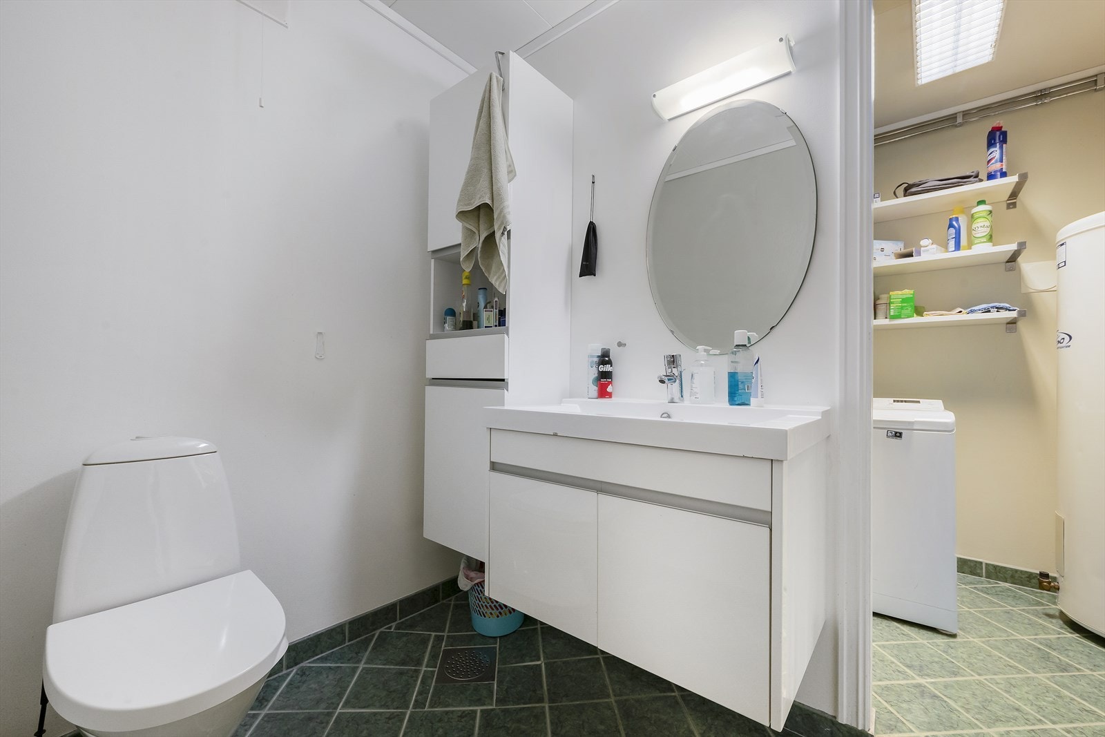 Badet har flislagt gulv m/varmekabler og baderomsmøbel med heldekkende servant og skap. Videre er det gulvmontert toalett, dusjkabinett og opplegg for vaskemaskin. Galleribilde