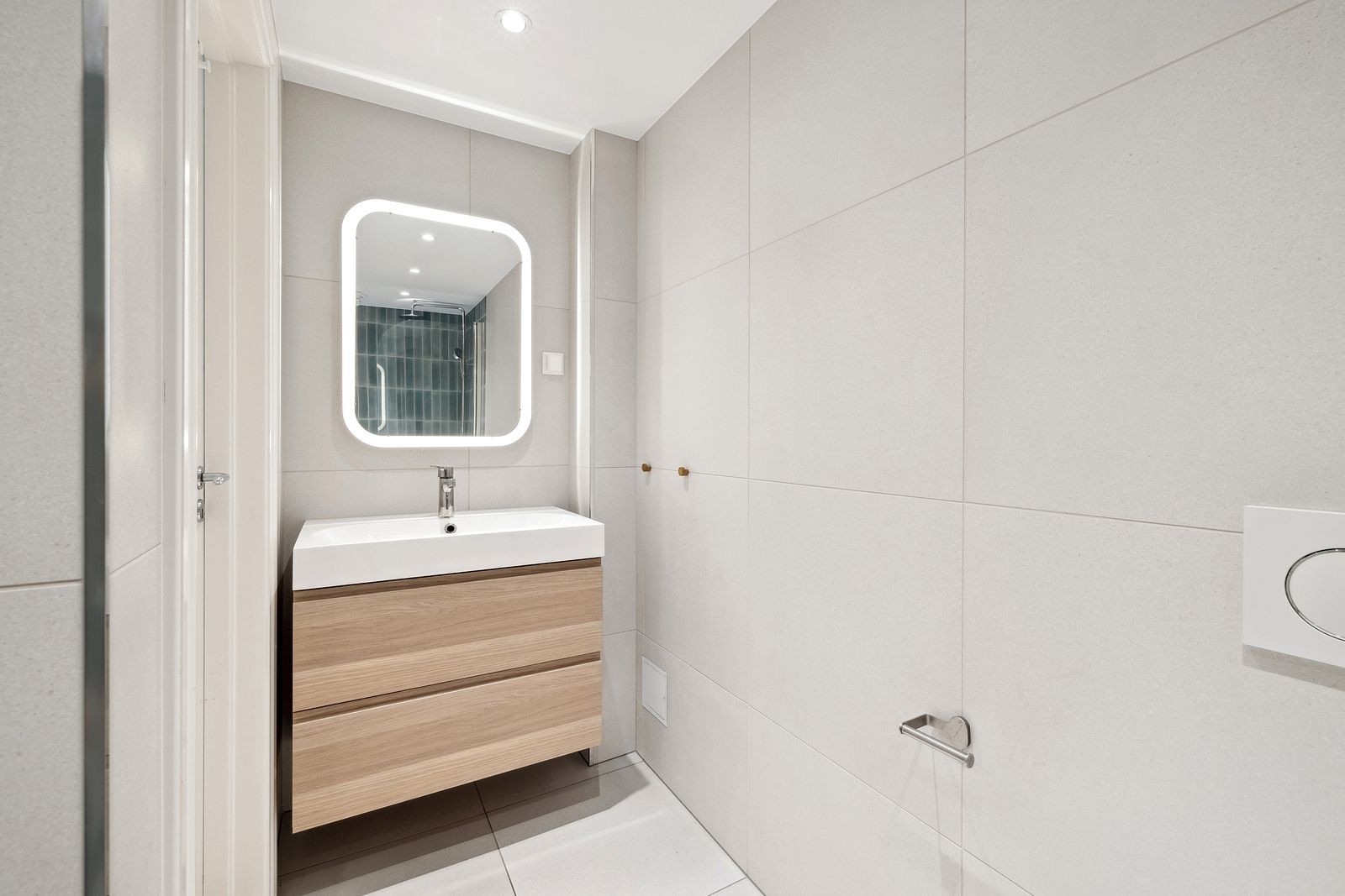 Badet har vegghengt toalett, pent servantmøbel og ledlys-speil. Galleribilde