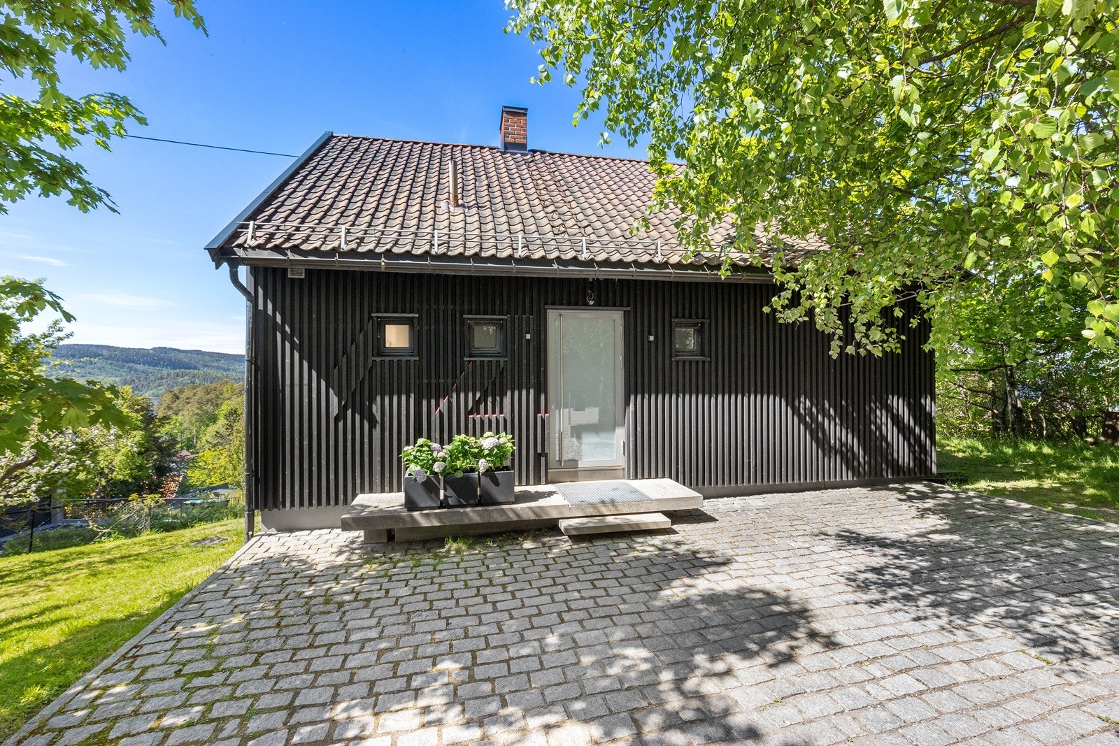 Steinbelagt gårdsplass og inngangsparti med biloppstillingsplasser. Galleribilde